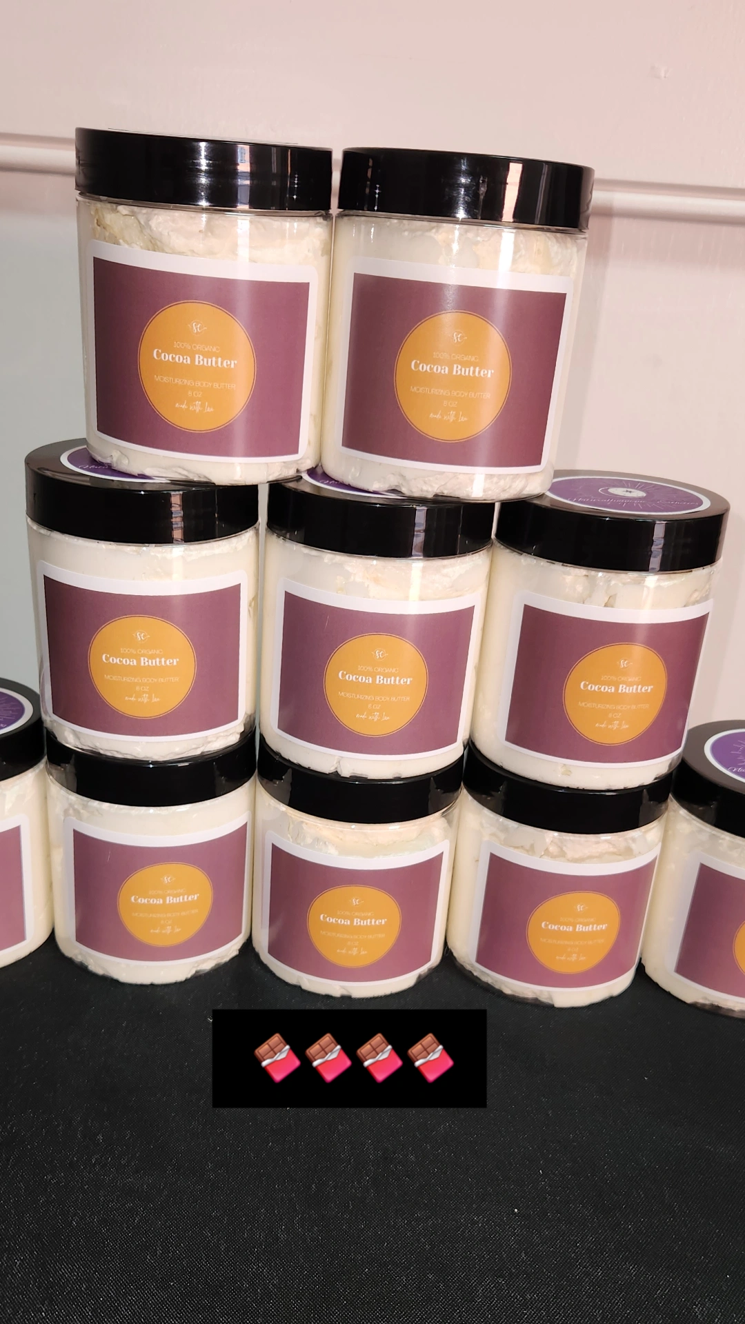 Nine containers with black lids and purple labels stacked on a black surface, with small pink objects below.