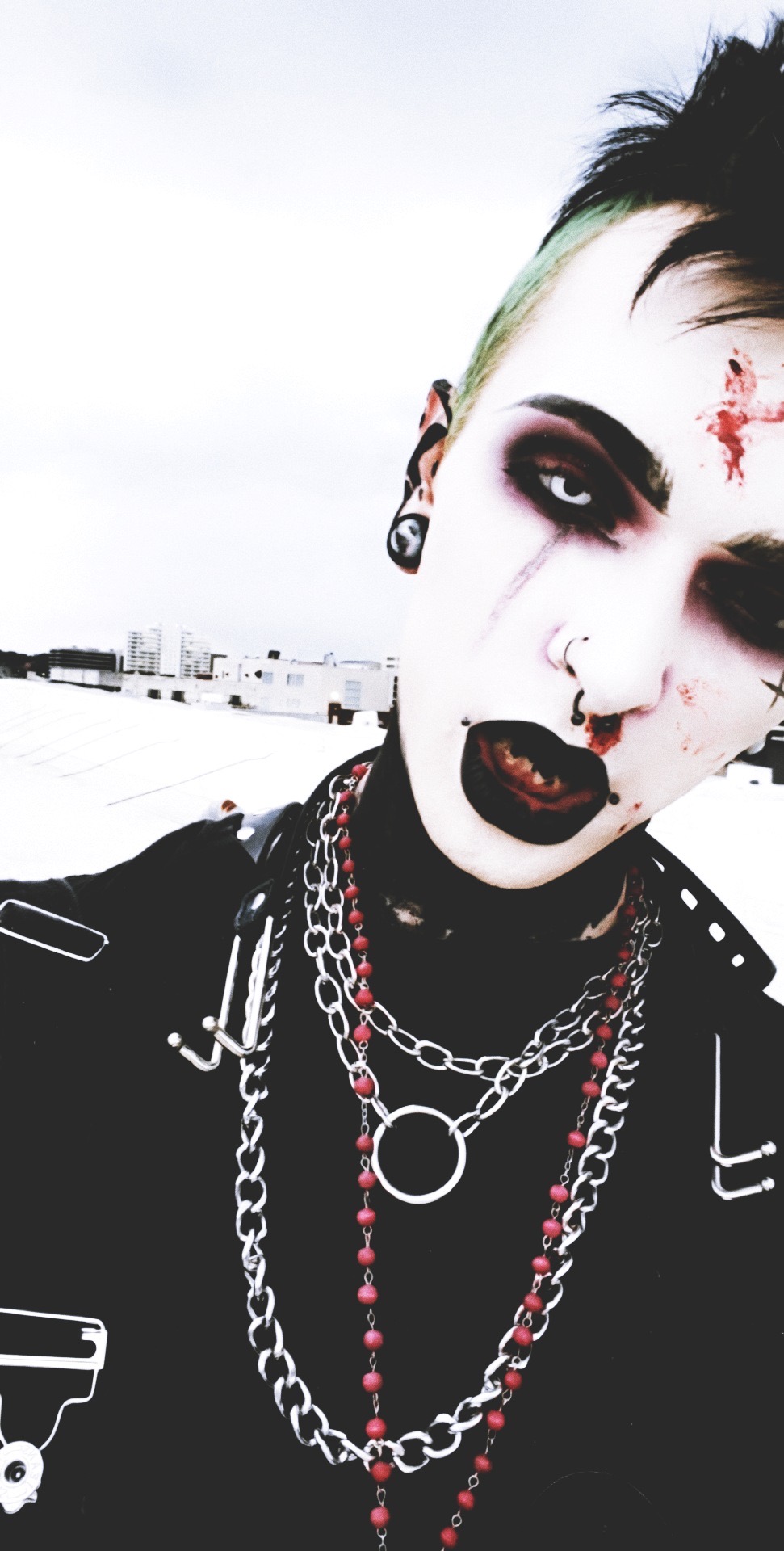 Person with dark makeup, piercings, and chains, outdoors with a cloudy sky background.