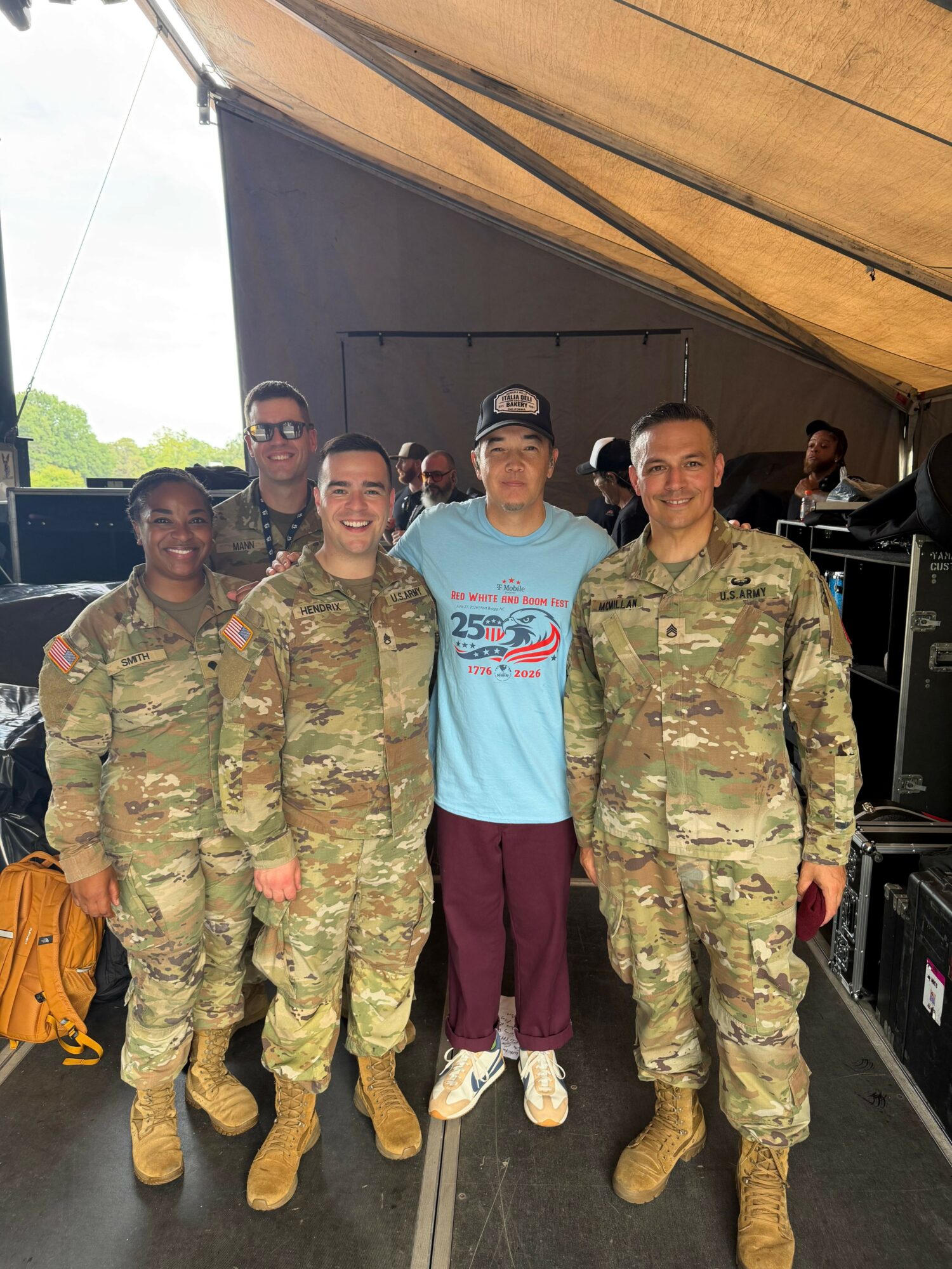 Group of people, including soldiers in camouflage uniforms, standing indoors with a person in casual clothing, some wearing masks.