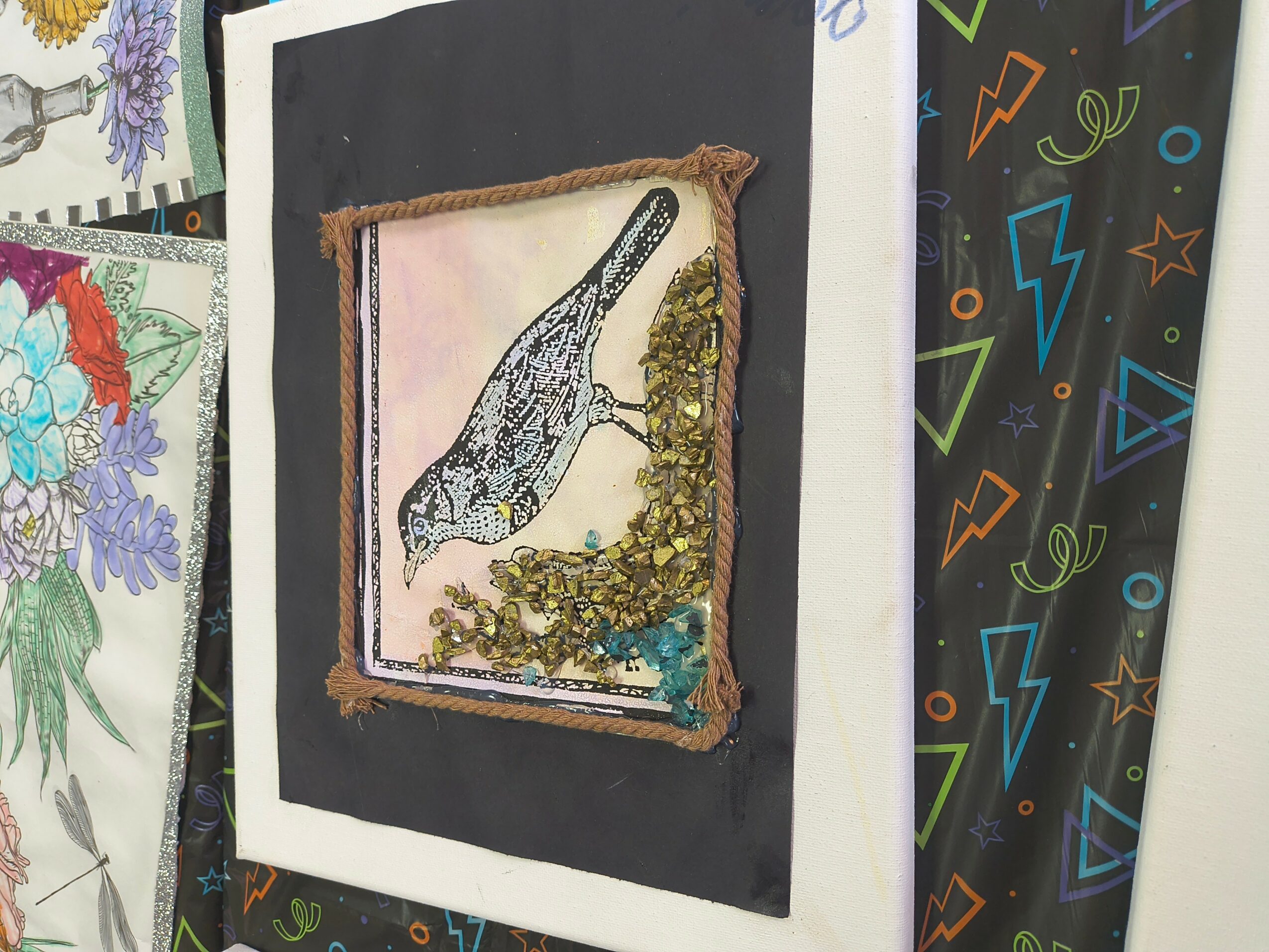 Framed artwork of a dinosaur with gold embellishments on a black background, displayed on a wall with colorful patterns.