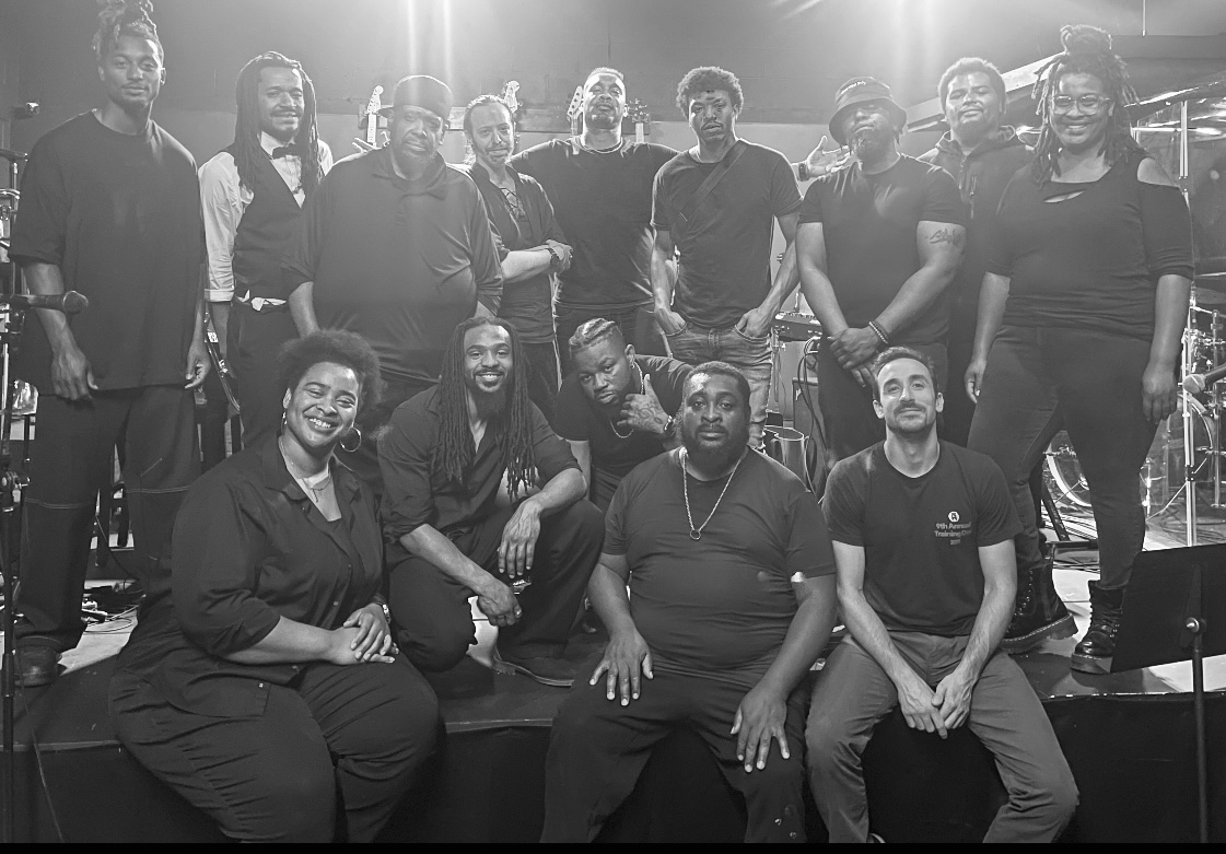 Group of people posing together on stage, some sitting and some standing, in a black and white photo.