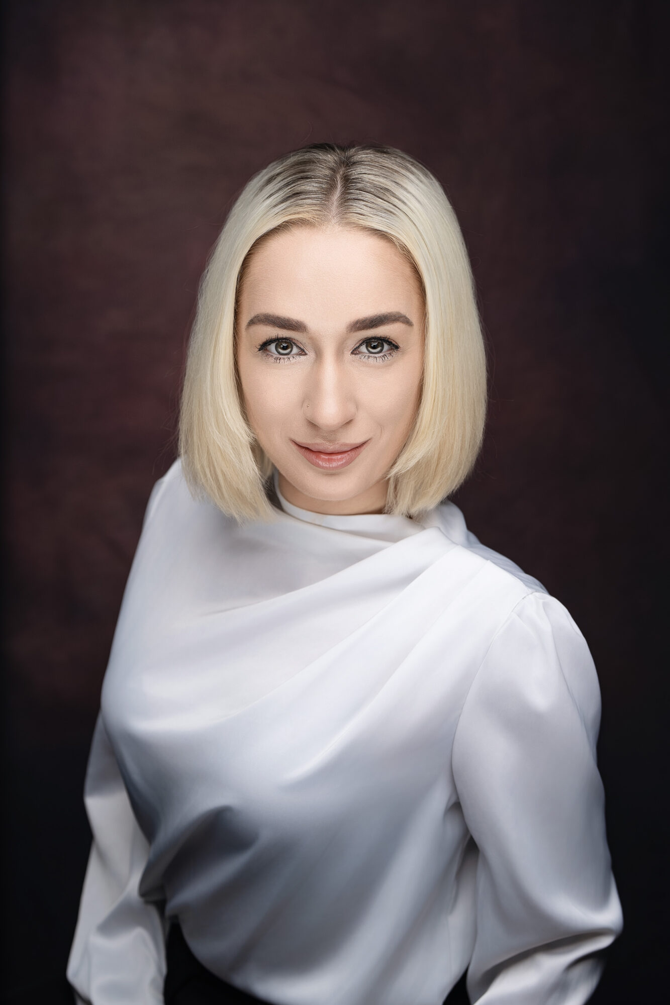 Young woman with blonde hair and a white top, smiling softly, against a dark background.
