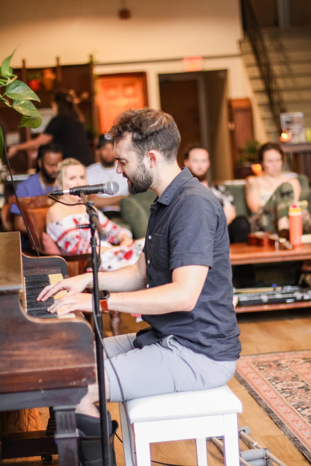 Young man playing piano in a lively indoor setting with people in the background.