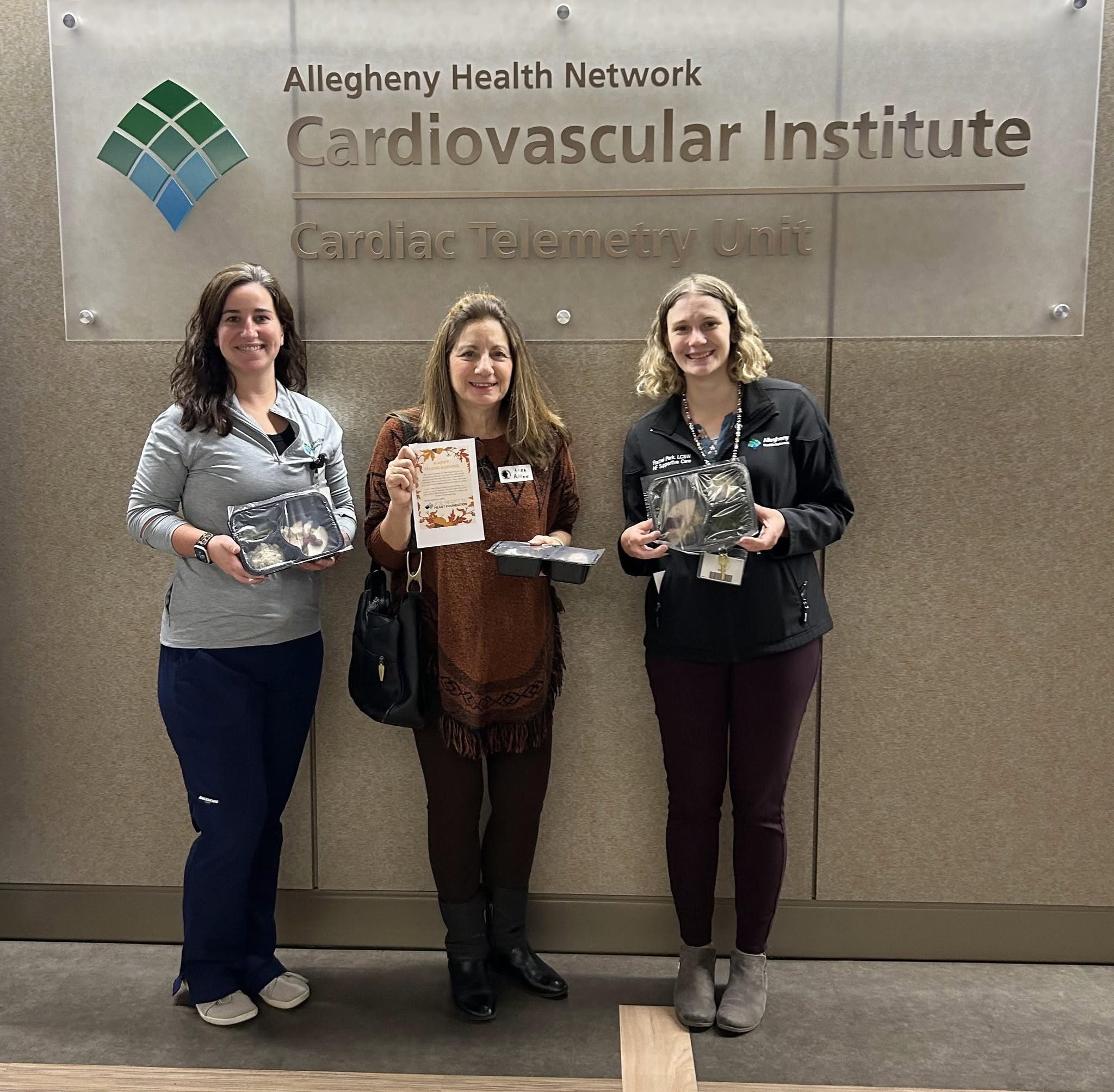 Three women stand in front of a sign for the Cardiovascular Institute at Allegheny Health Network, holding awards or plaques.