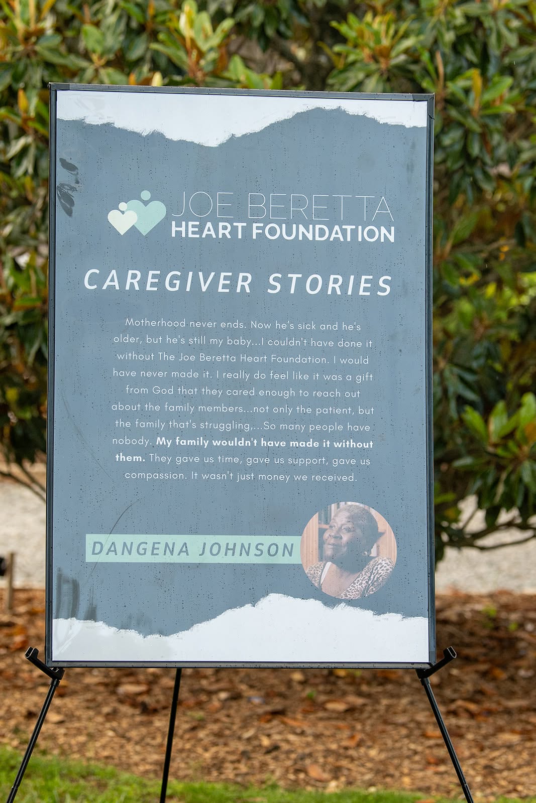 Informational sign about Joe Beretta Heart Foundation and caregiver stories, with a photo of a person, outdoors with greenery.