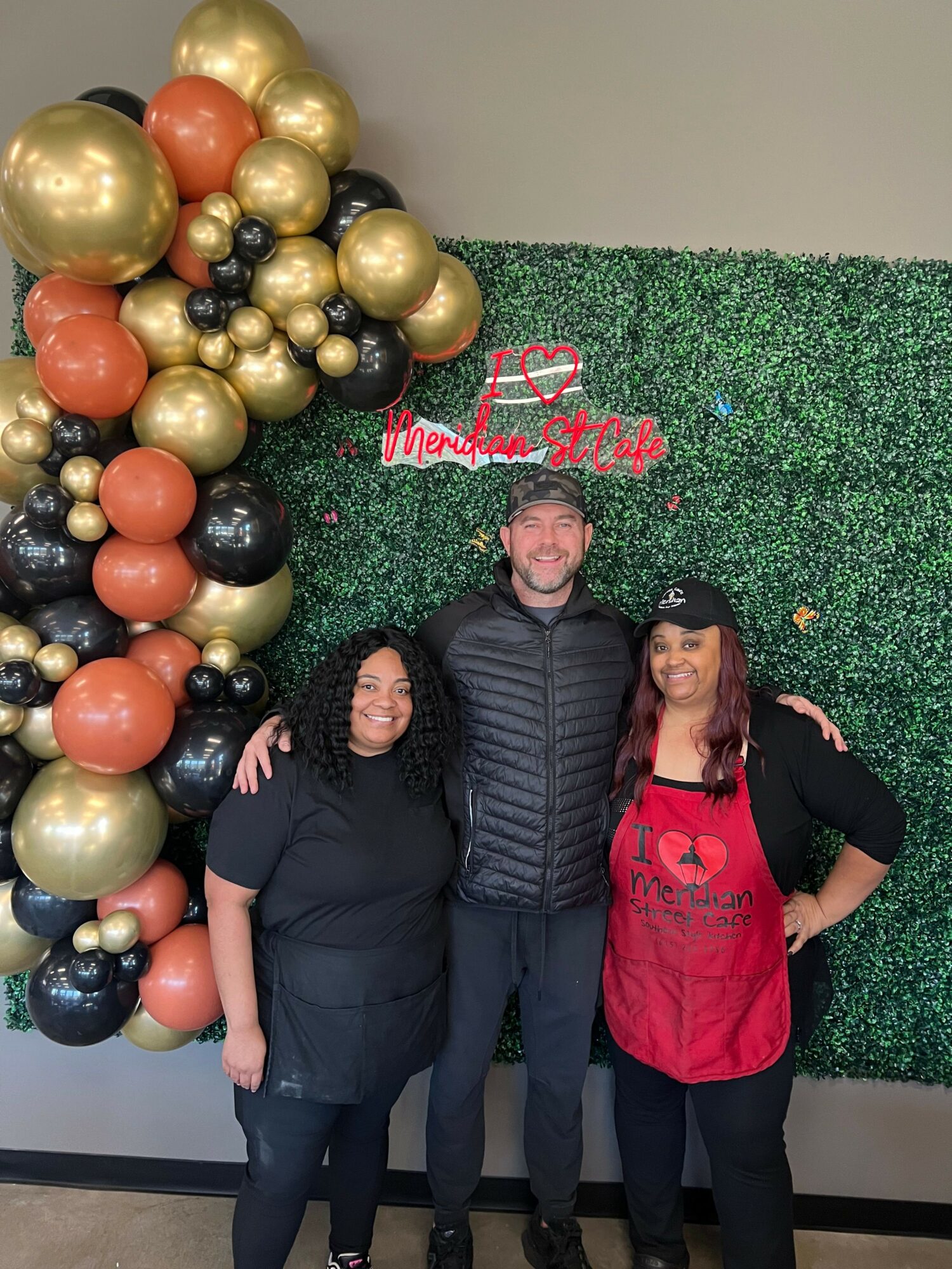 Three people lying on artificial grass with Christmas decorations and balloons, smiling at the camera.