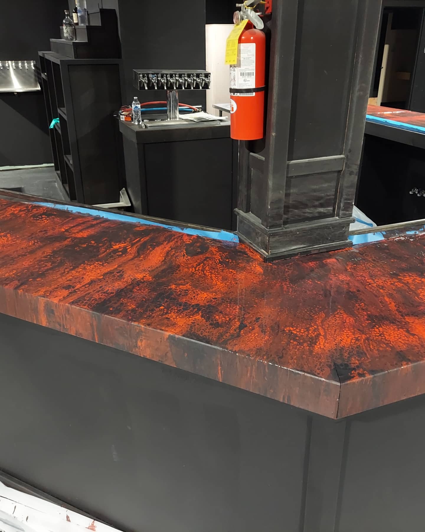 Countertop with a red and black marbled pattern, black base, and a black vertical structure in the background with a fire extinguisher attached.