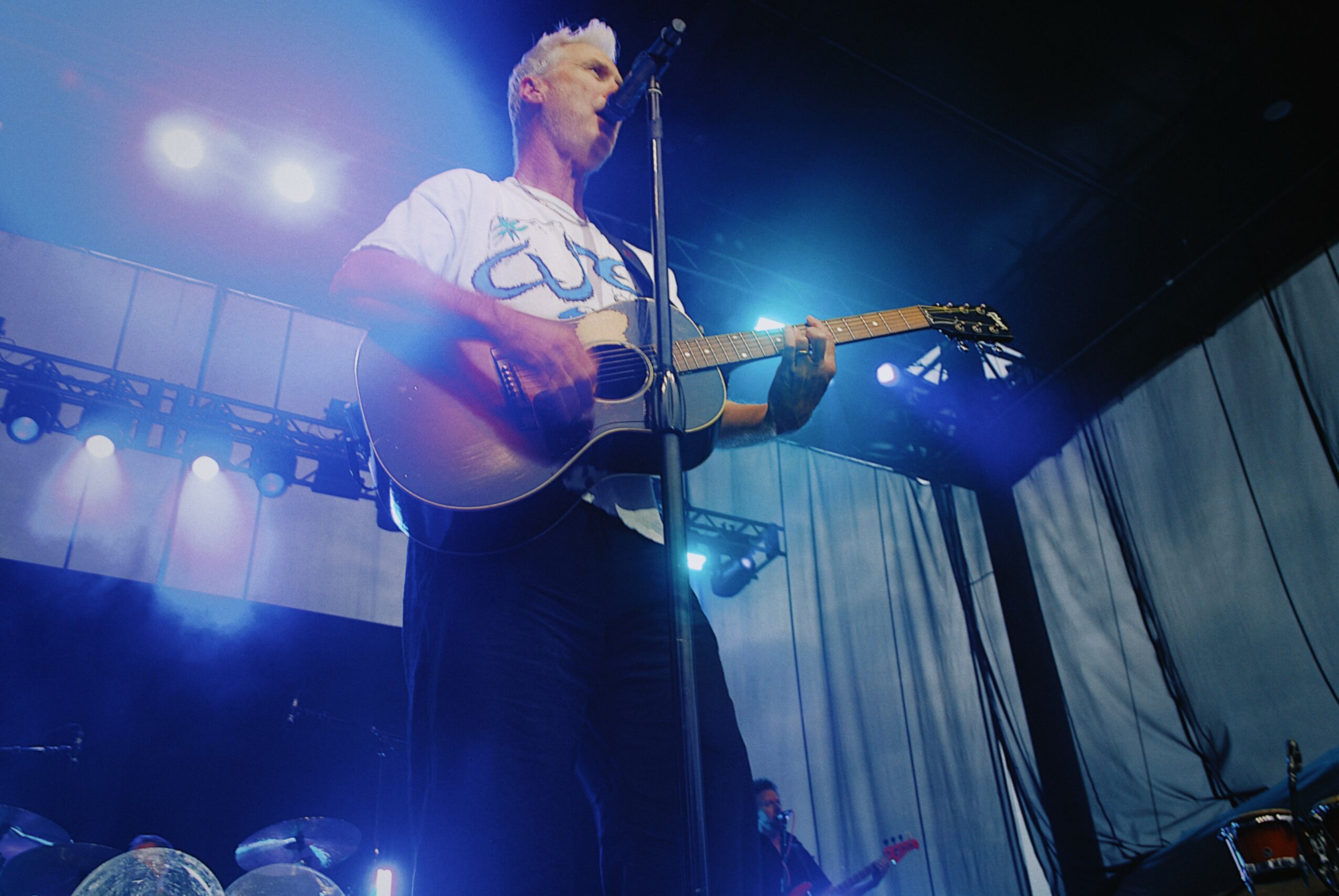 Person playing guitar on stage with bright lights and curtains in background