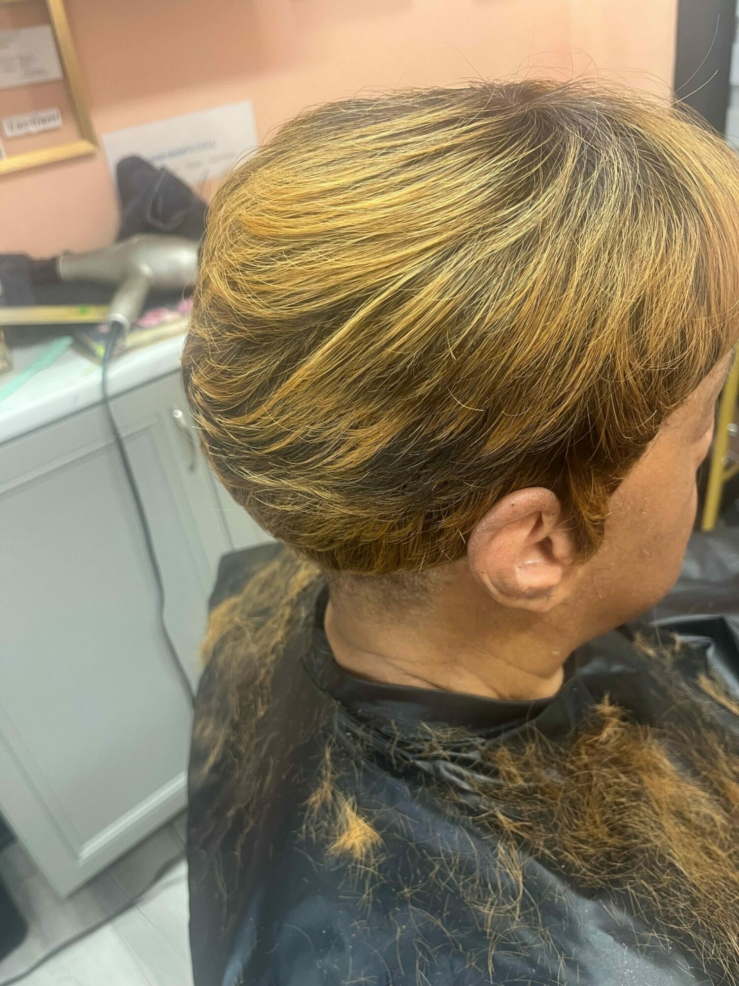 Person with light brown hair sitting in a salon chair, facing downward, with hair covering their face.