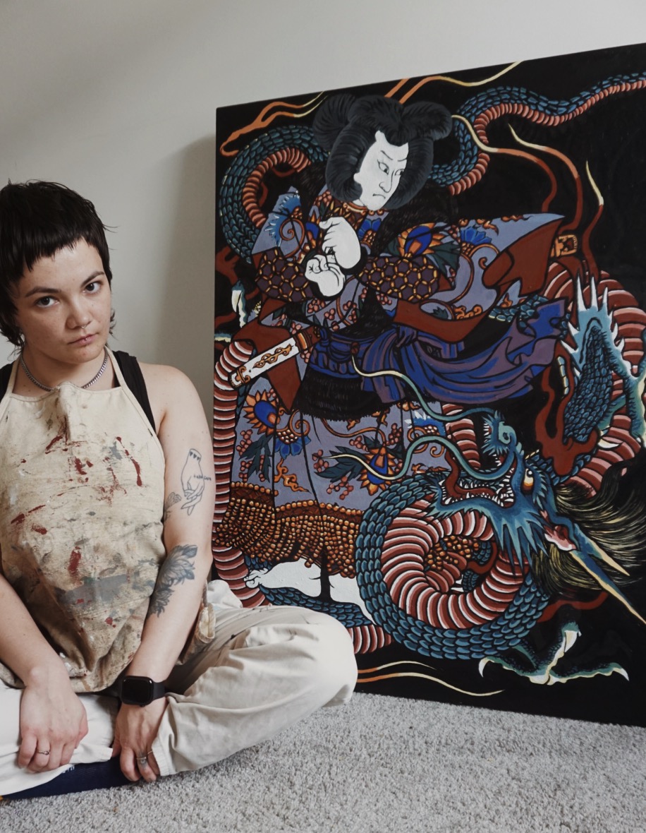 Person sitting on floor next to a large colorful painting of a woman with snakes and animals, in a room with gray carpet.