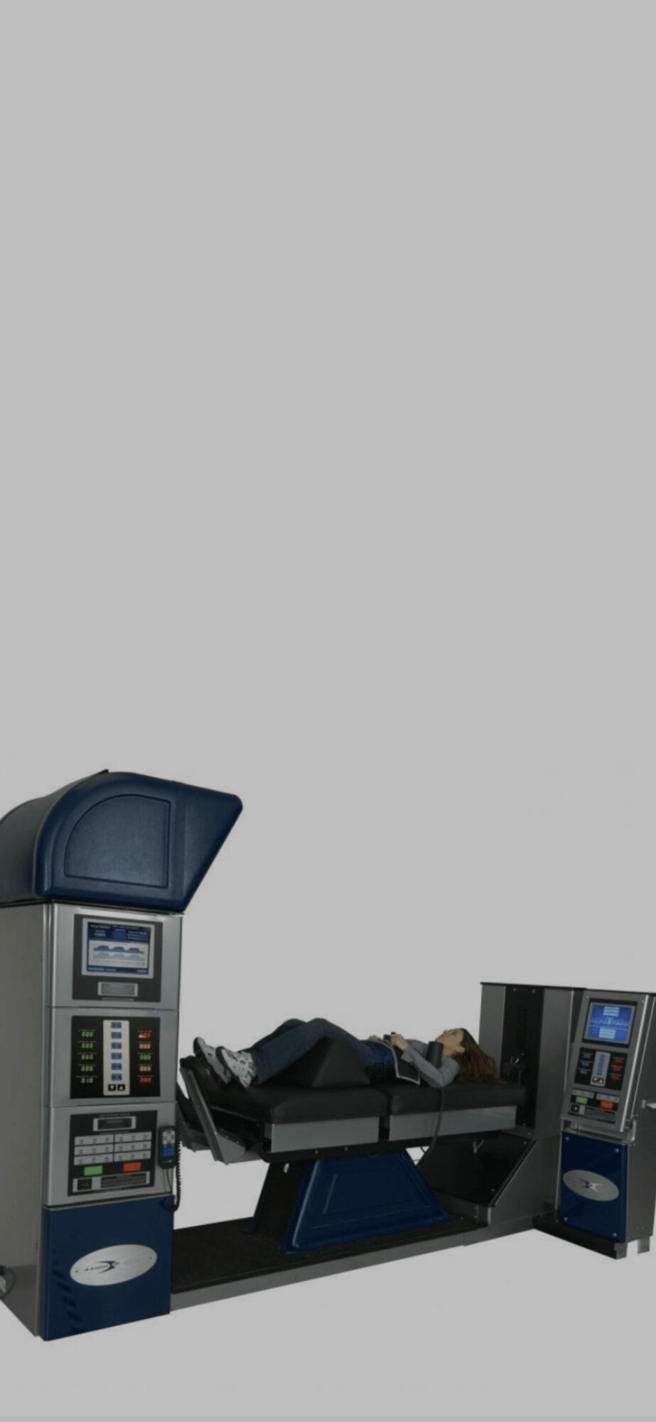 Person lying on a medical or laboratory examination table with equipment on both sides, against a plain background.