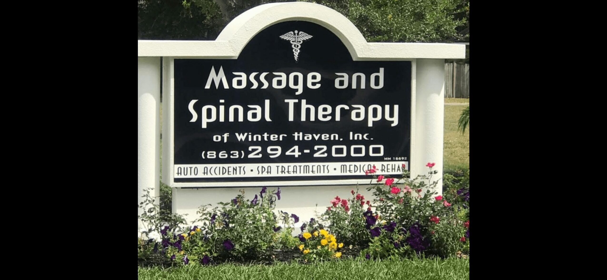 Sign for massage and spinal therapy with contact information and flowers at the base.