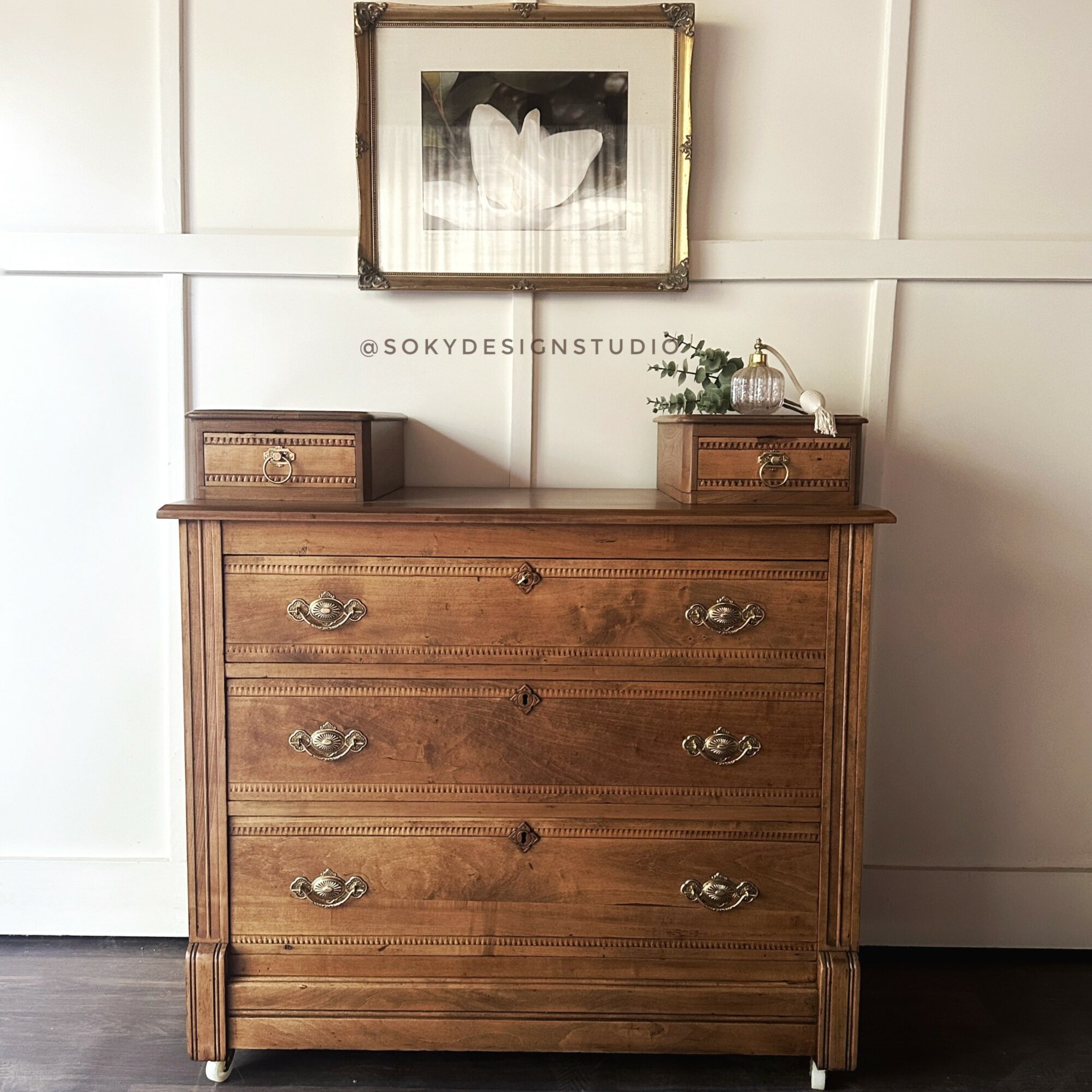 Wooden dresser with four drawers, decorative handles, and a framed black-and-white flower picture above it.