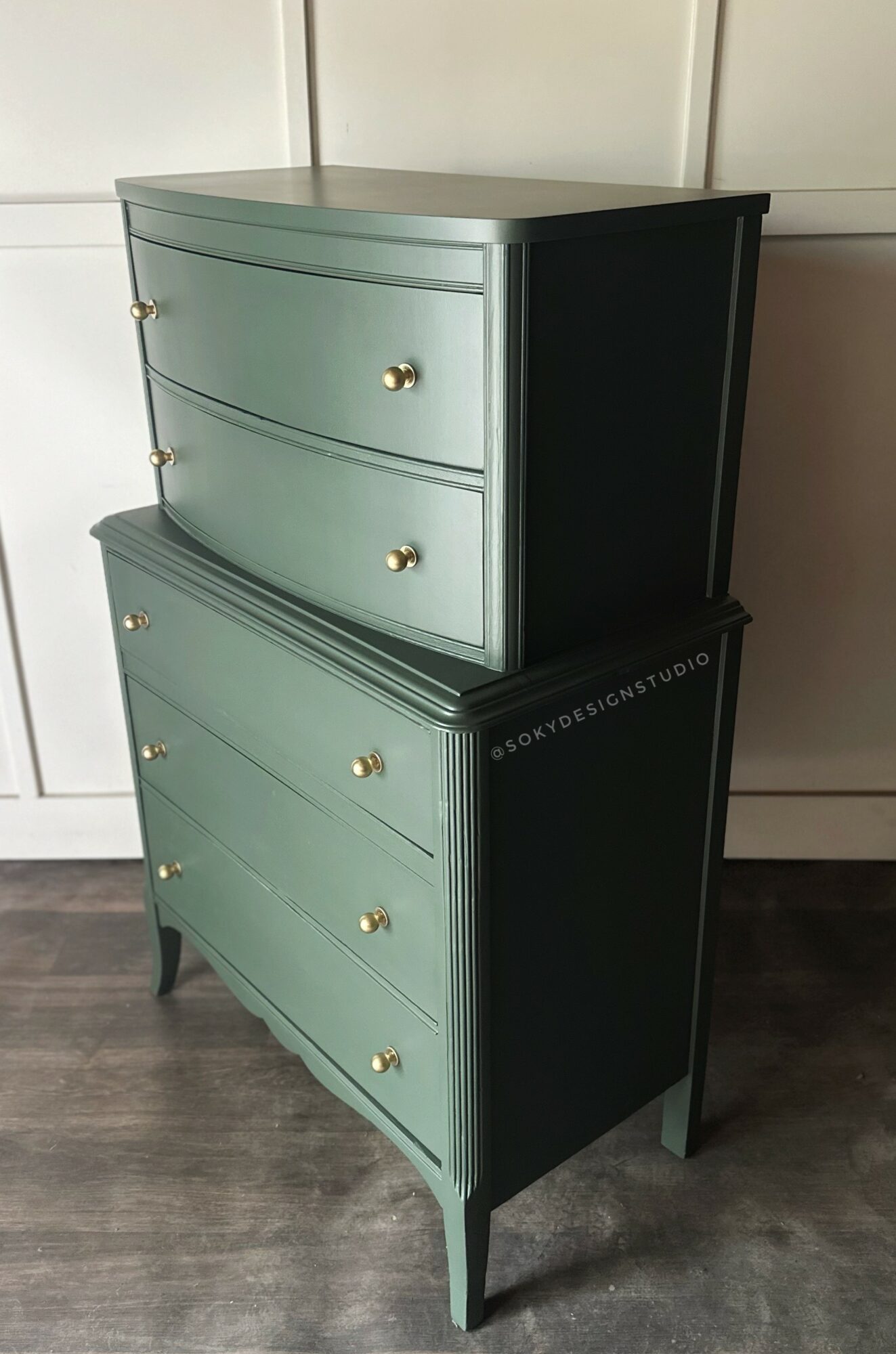Two-tone dresser with three drawers on top and three larger drawers below, gold knobs, and curved front, standing on a wooden floor.