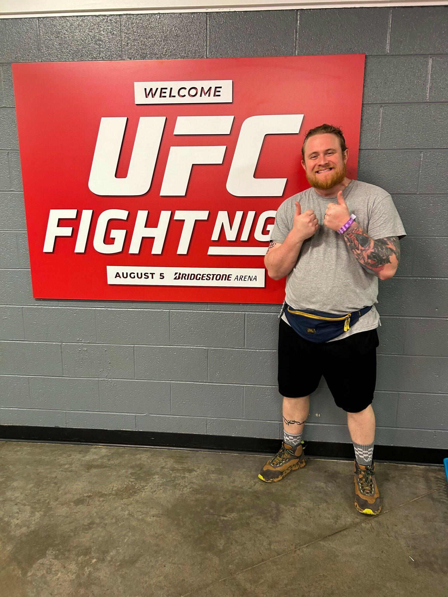 Person standing next to UFC Fight Night sign, holding a bag, in a hallway with gray walls and concrete floor.