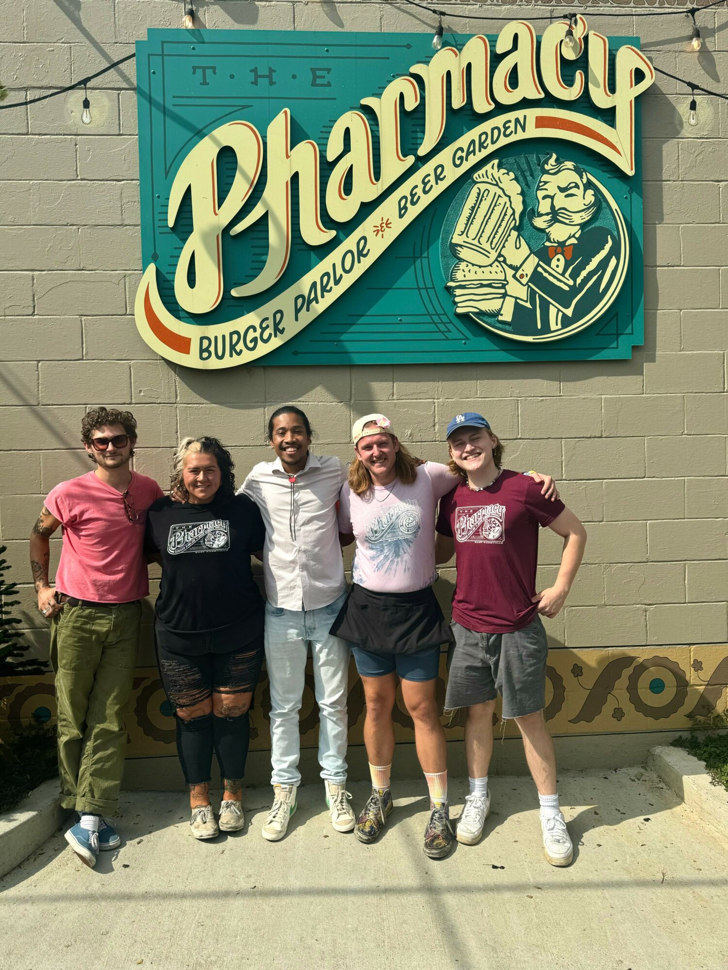Five people stand in front of a sign for a burger and beer garden, smiling and posing outdoors.