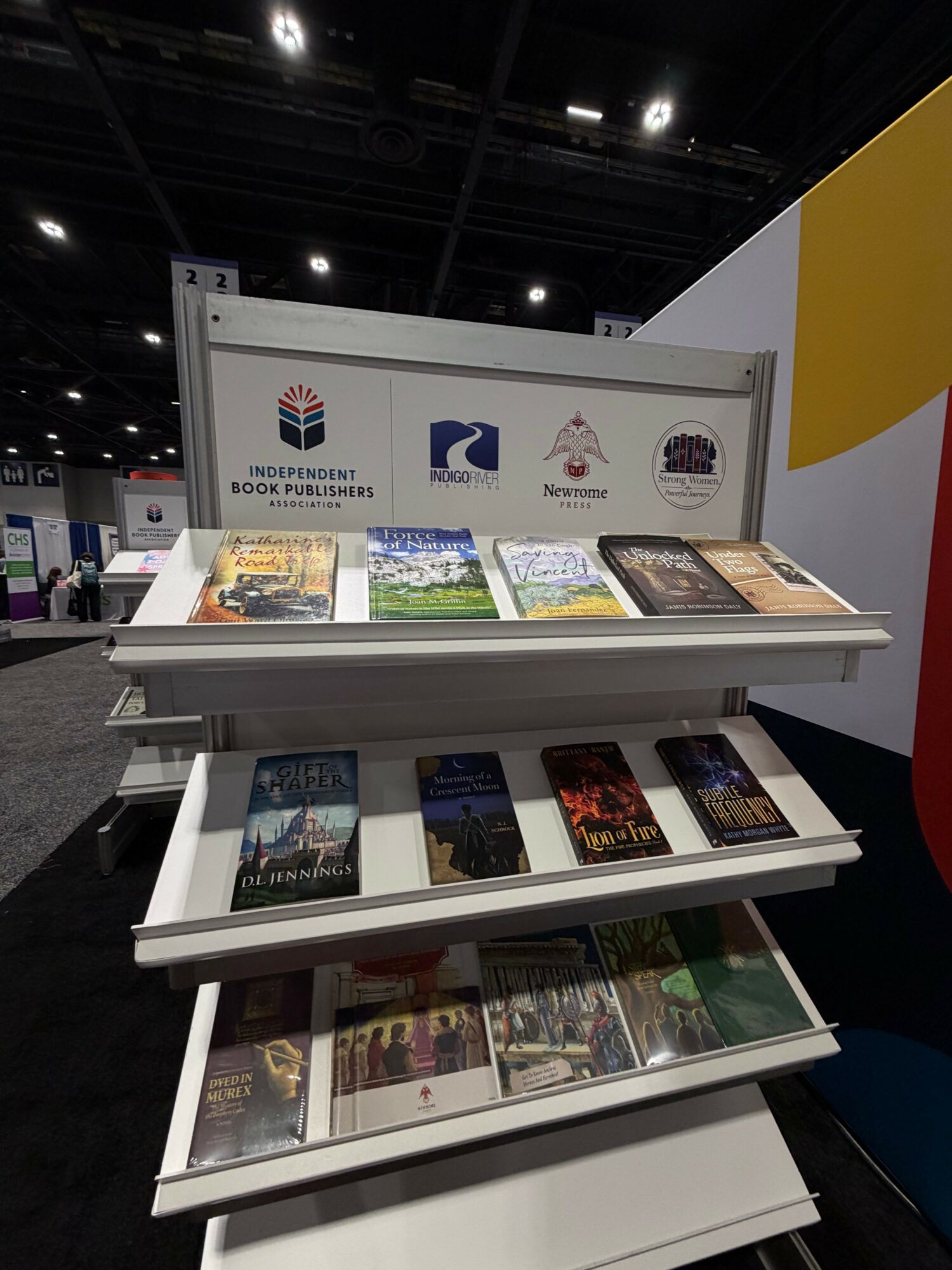 Display with brochures and posters, featuring logos and text, set in an indoor exhibition space with black curtains and ceiling lights.
