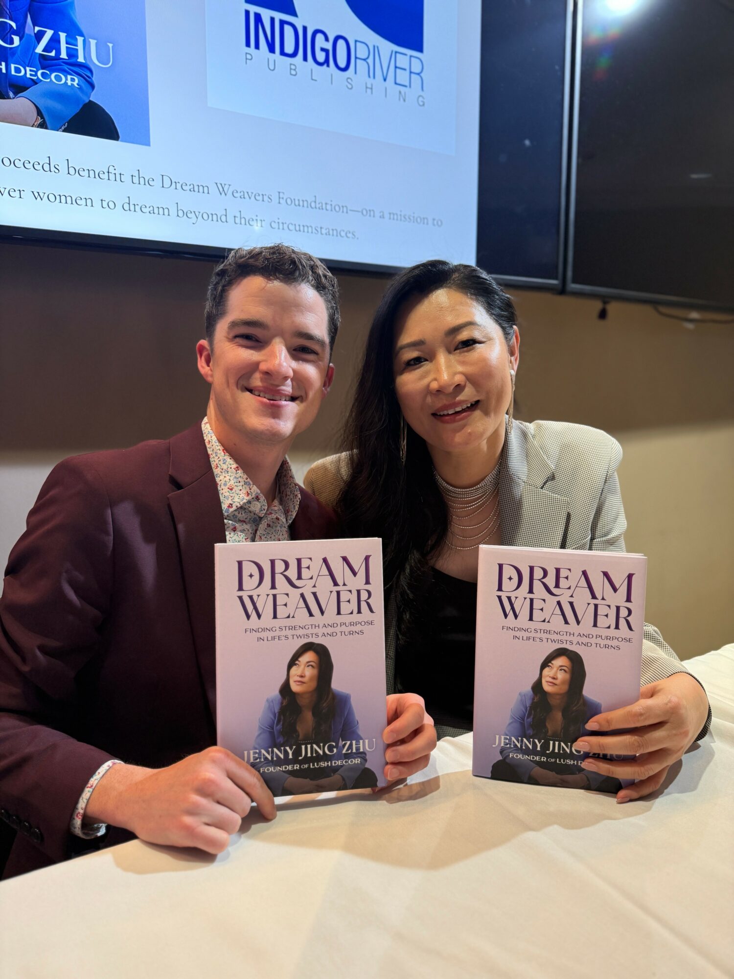 Two people sitting at a table holding books titled 'Dream Weaver' by Jenny Jing, smiling at the camera.