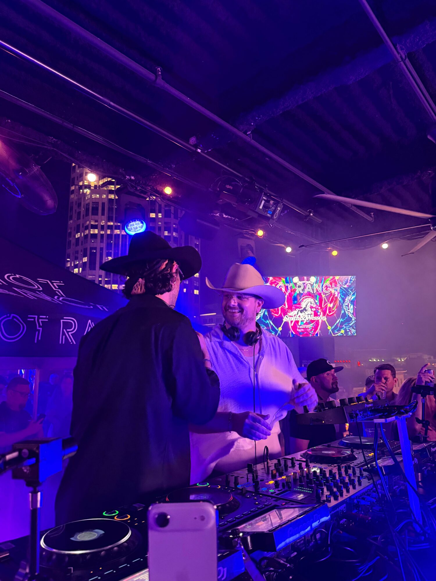 People dancing on a stage with colorful lights and a large screen in the background.