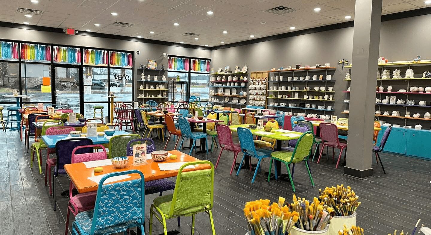 Colorful tables and chairs inside a store with shelves of products and flowers in the foreground.