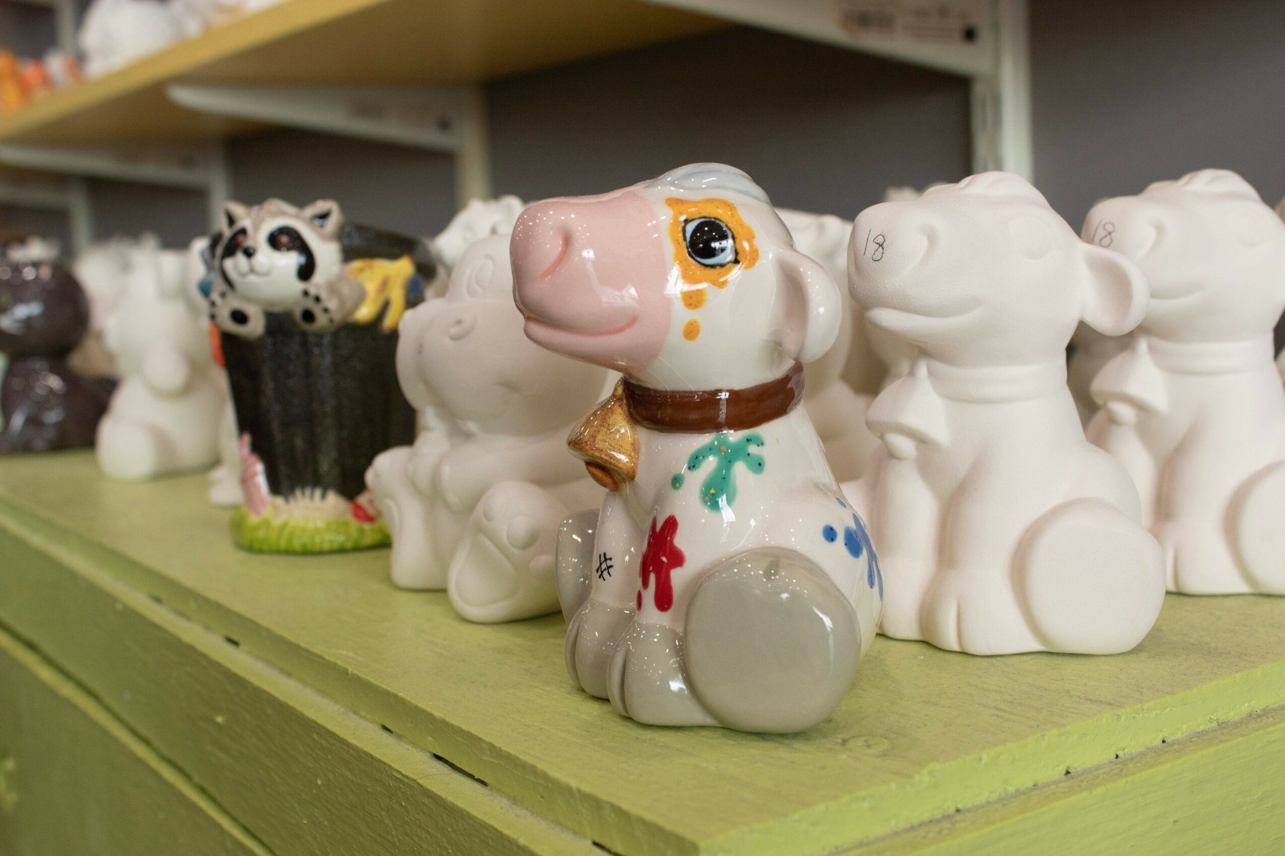 Decorative ceramic dog figurine with painted details, surrounded by plain white dog figurines on a green shelf.
