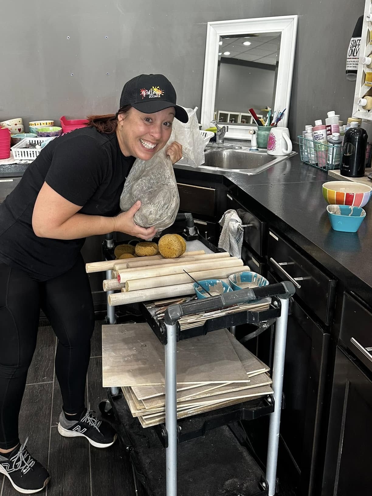 Person smiling, holding a large rock, standing in a kitchen with various supplies and a mirror in the background.