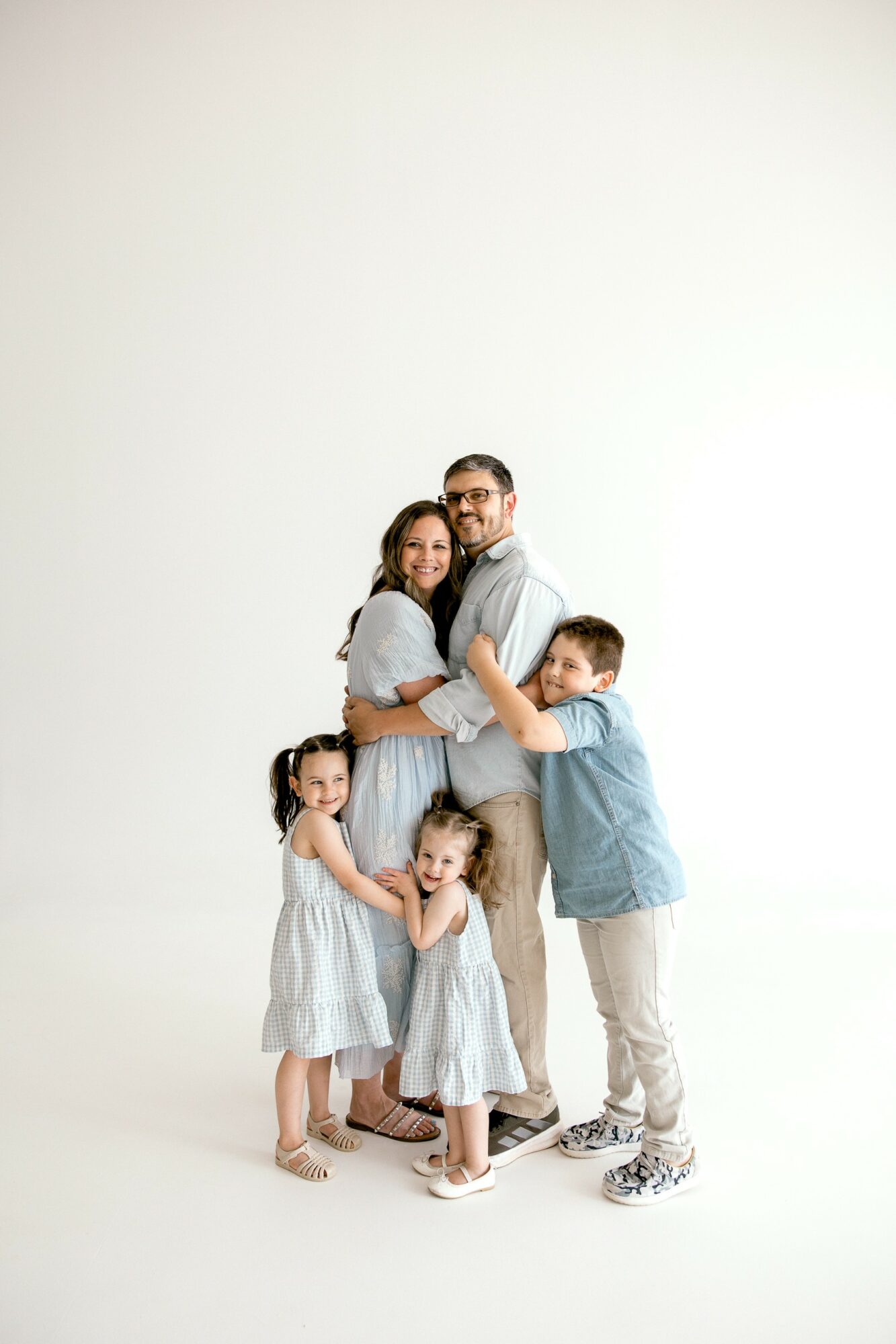 Family of five standing together, smiling, with a plain white background.