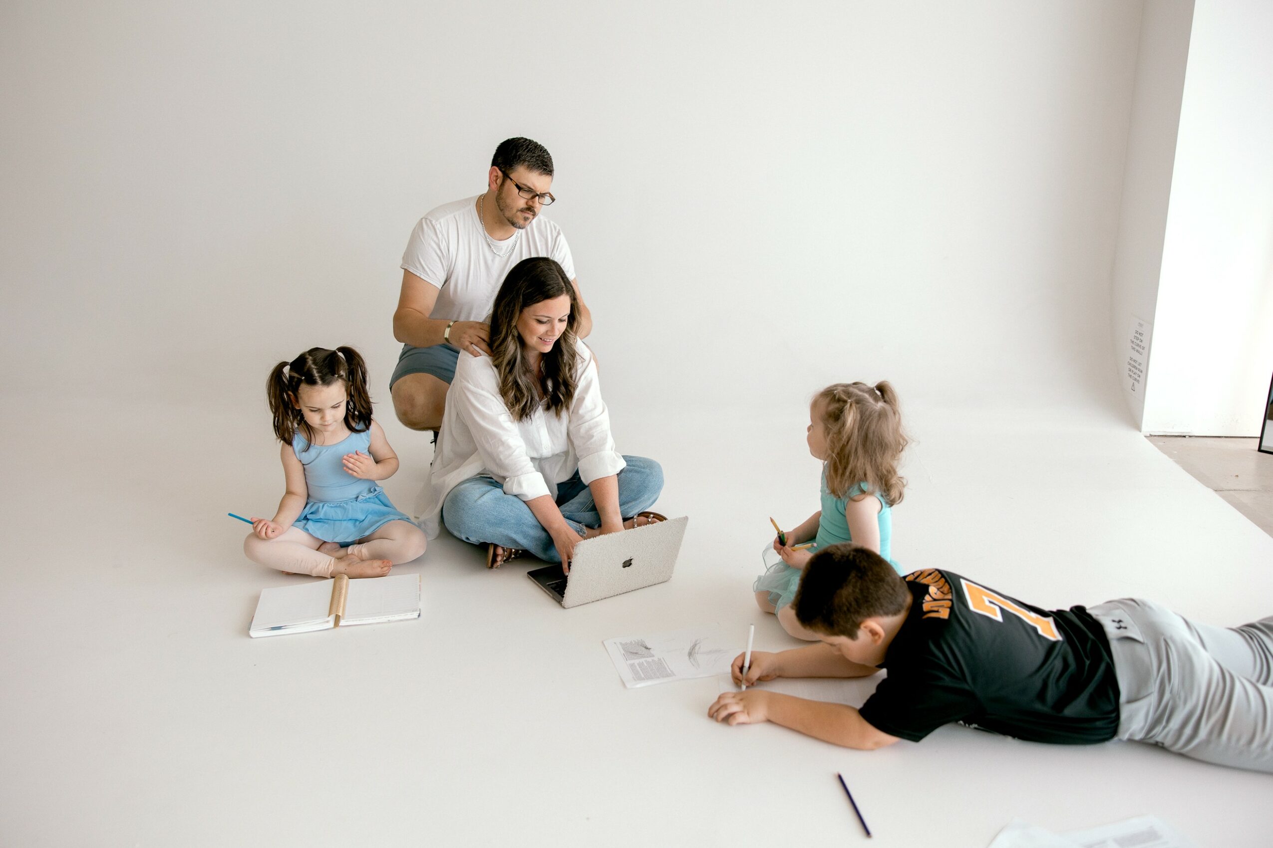Family of five sitting on the floor with a laptop, children and adults engaging in activity, bright room with natural light.