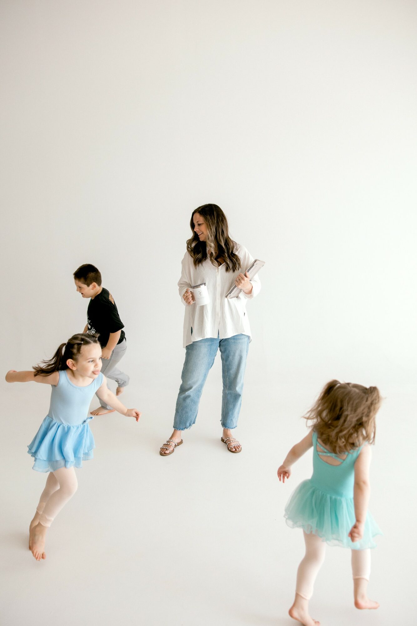 Woman and three children in ballet costumes and casual clothing in a studio with a plain white background.
