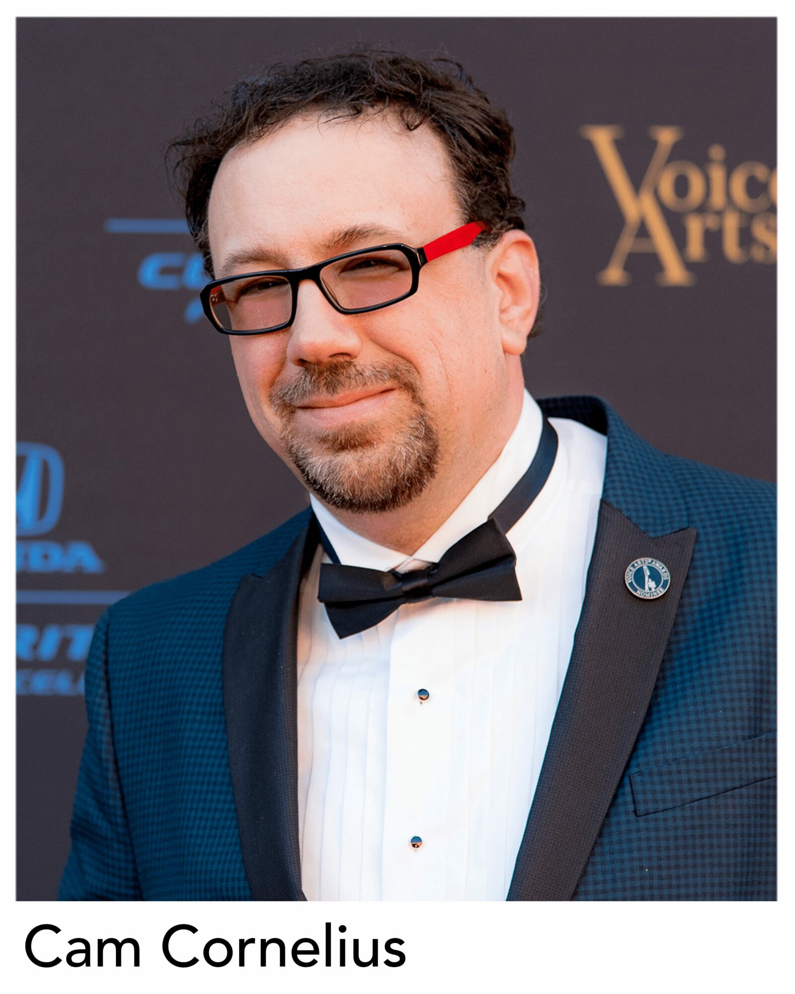 Man in tuxedo with glasses and bow tie, smiling, at an event backdrop, named Cam Cornelius.