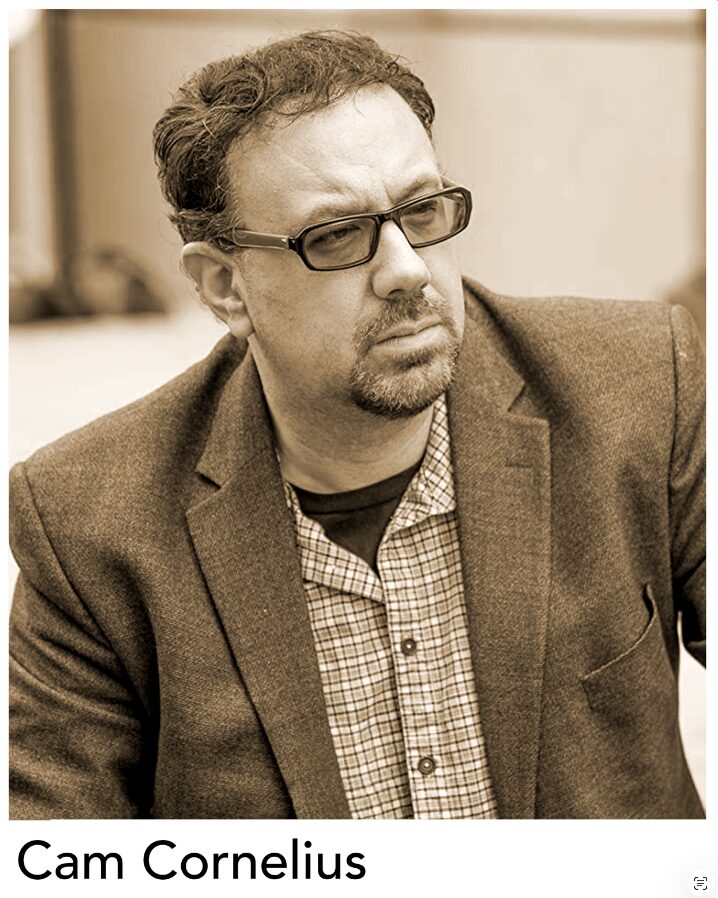 Man with glasses, beard, and mustache wearing a blazer and checkered shirt, looking to the side, in sepia tone.