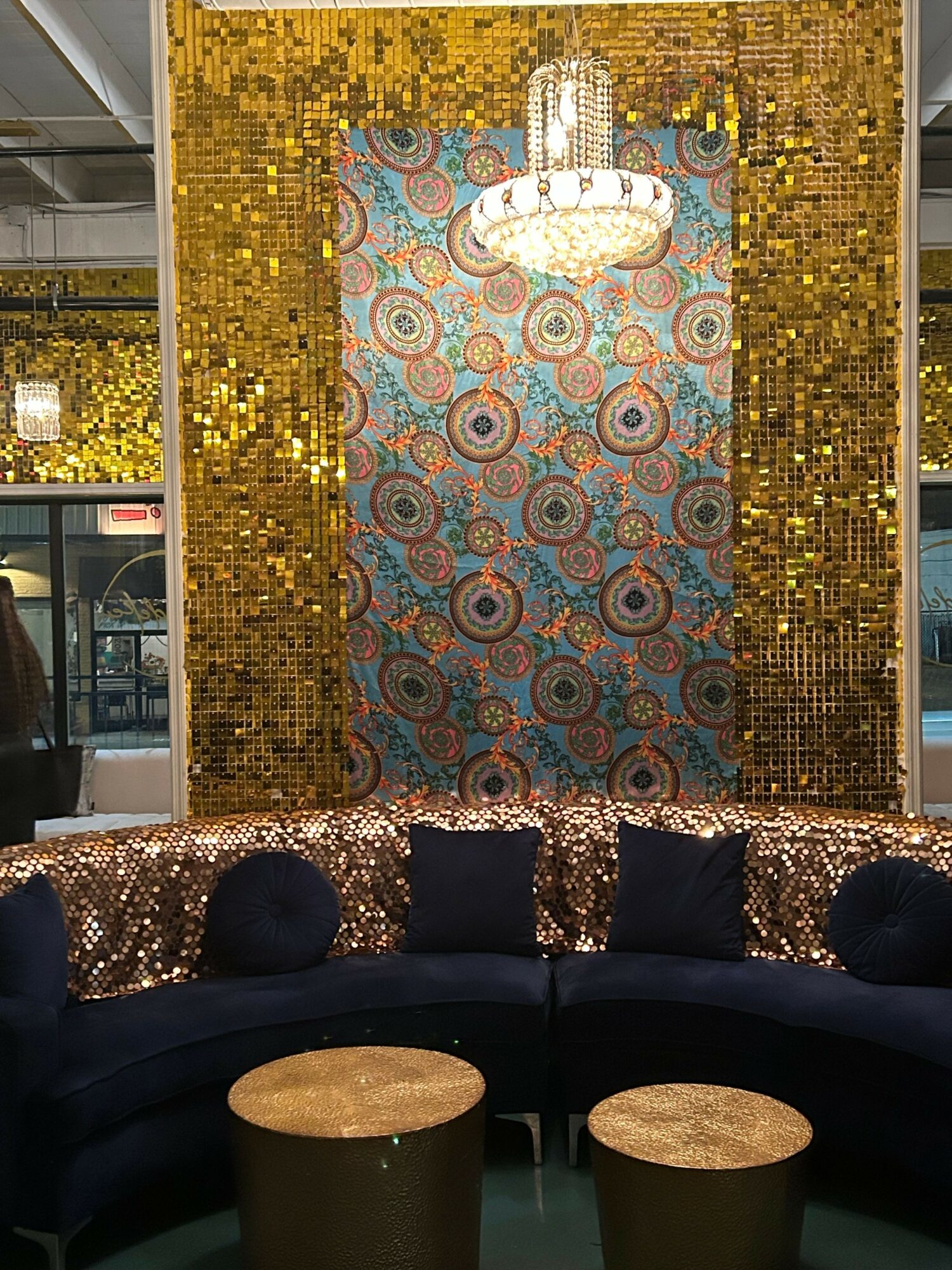 Decorative backdrop with gold sequins, circular patterned fabric, and a cloud-shaped sign, with a table and chairs in front.