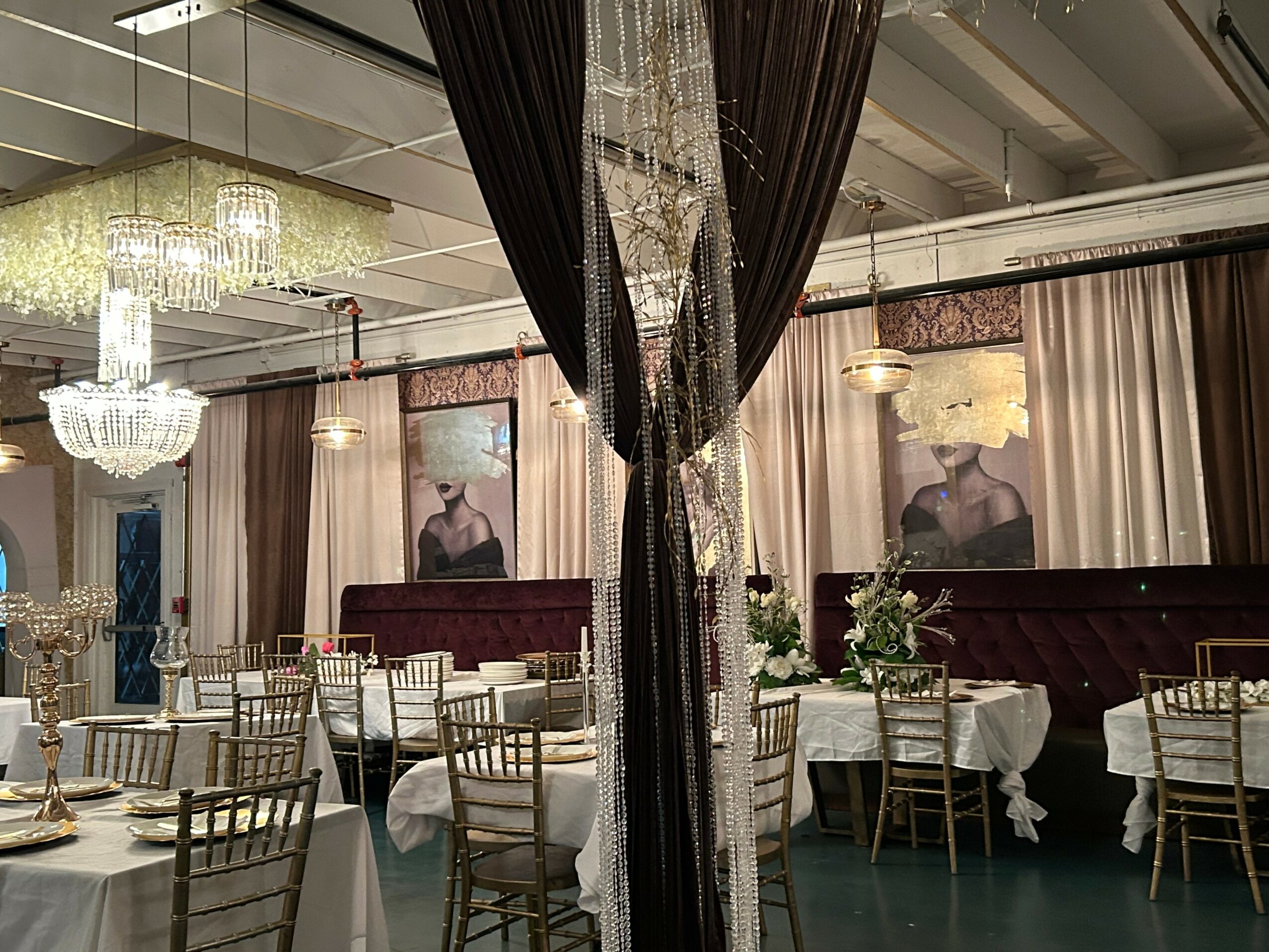 Elegant banquet hall with chandeliers, draped curtains, and round tables with white tablecloths and gold chairs.