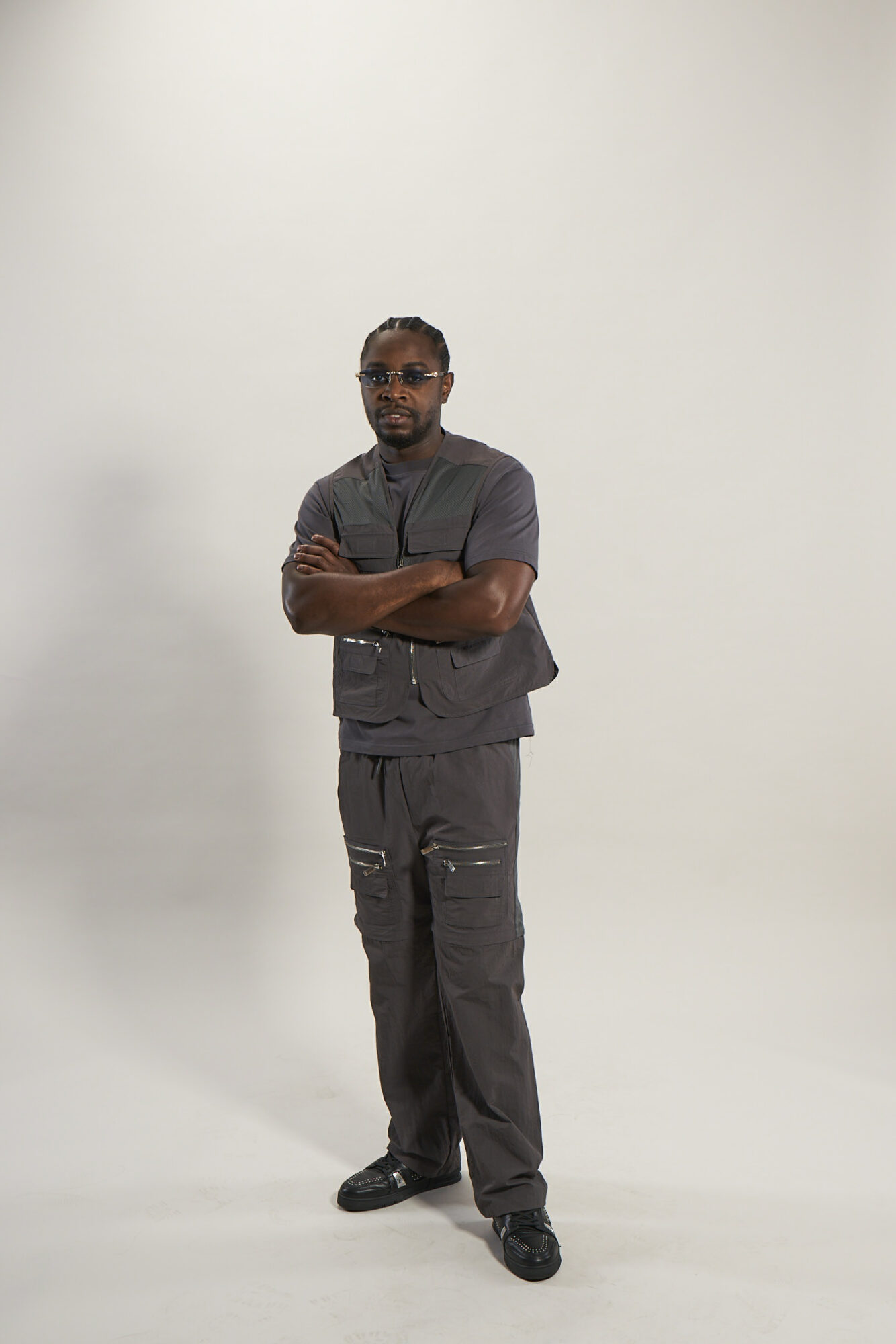 Man standing with arms crossed, wearing dark clothing, against a plain white background.