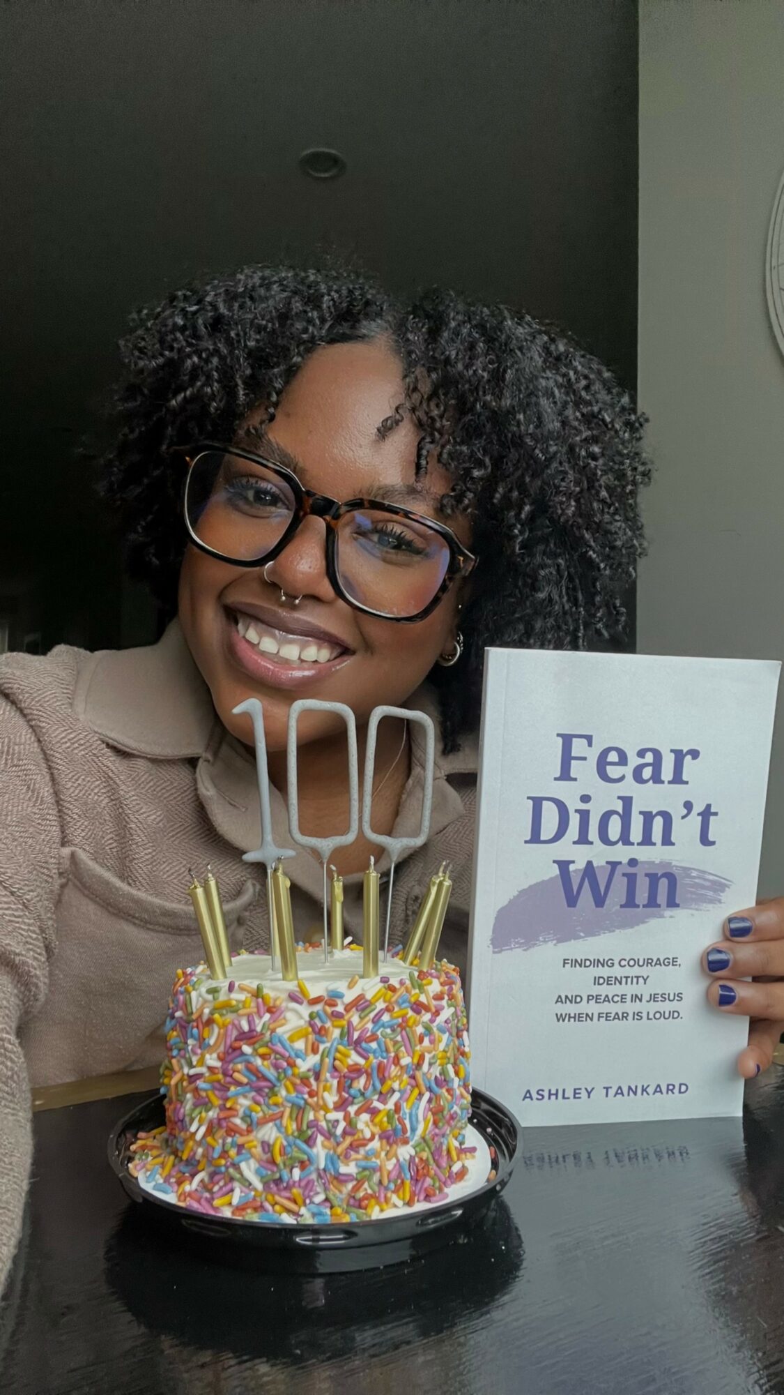 Smiling woman with glasses holding a book, celebrating with a colorful birthday cake with candles.