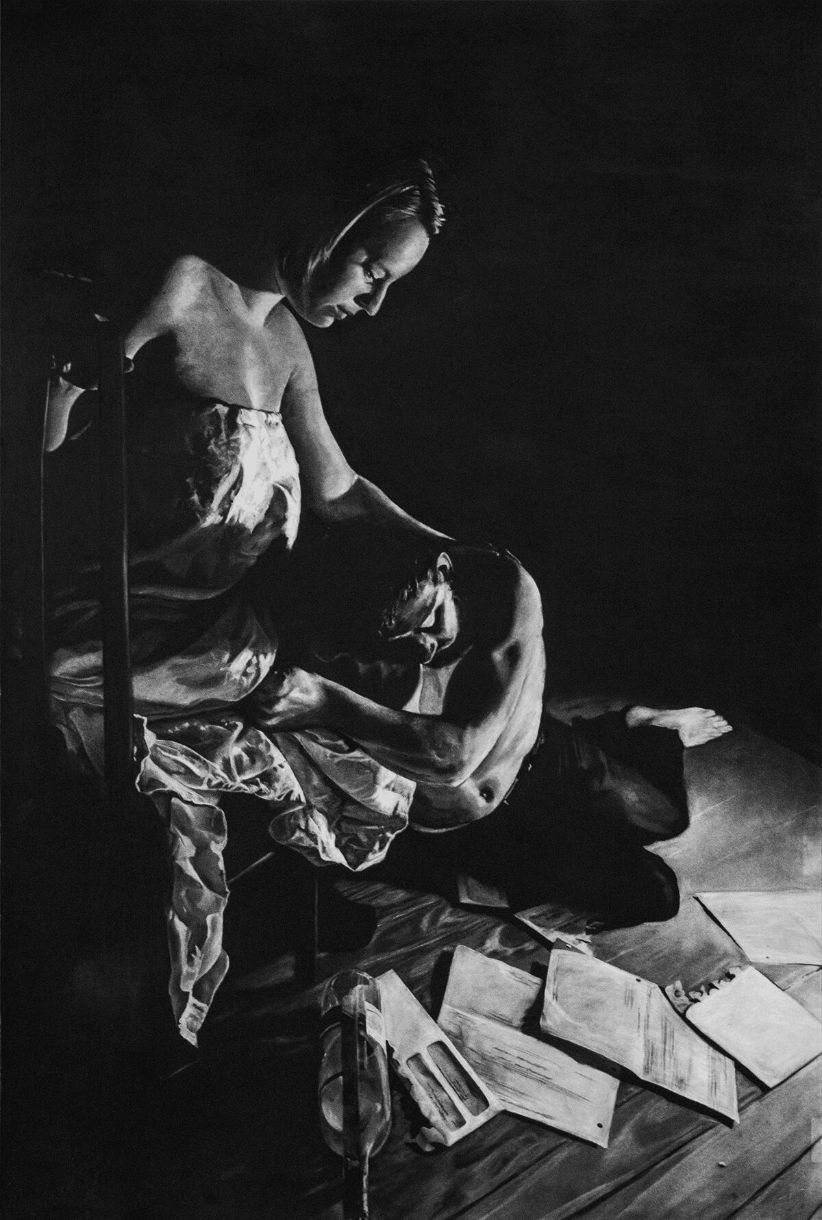 Two women sit together, one resting her head on the other's lap, surrounded by papers and books on a table.