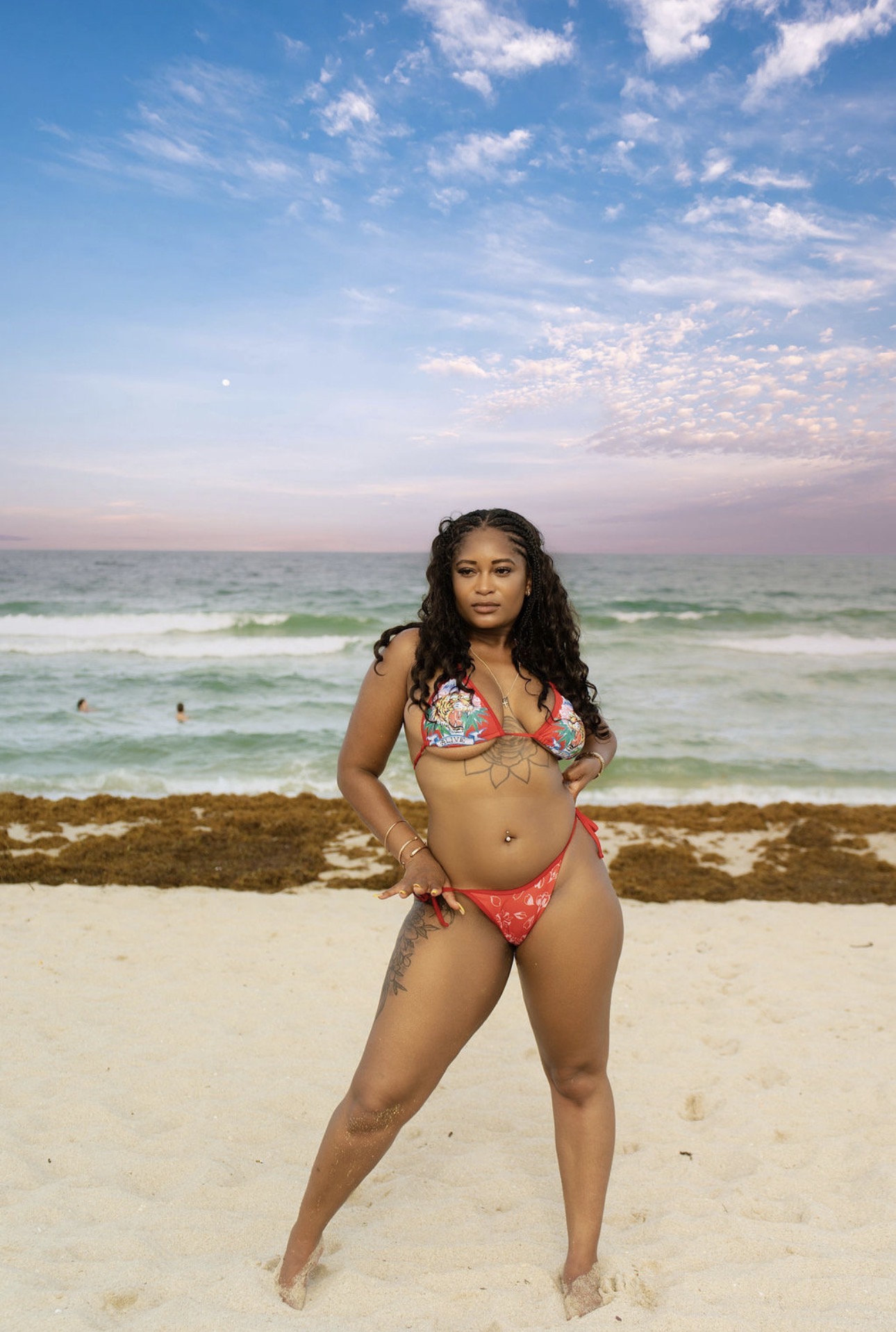 Woman in a bikini standing on a beach with ocean and sky in background.