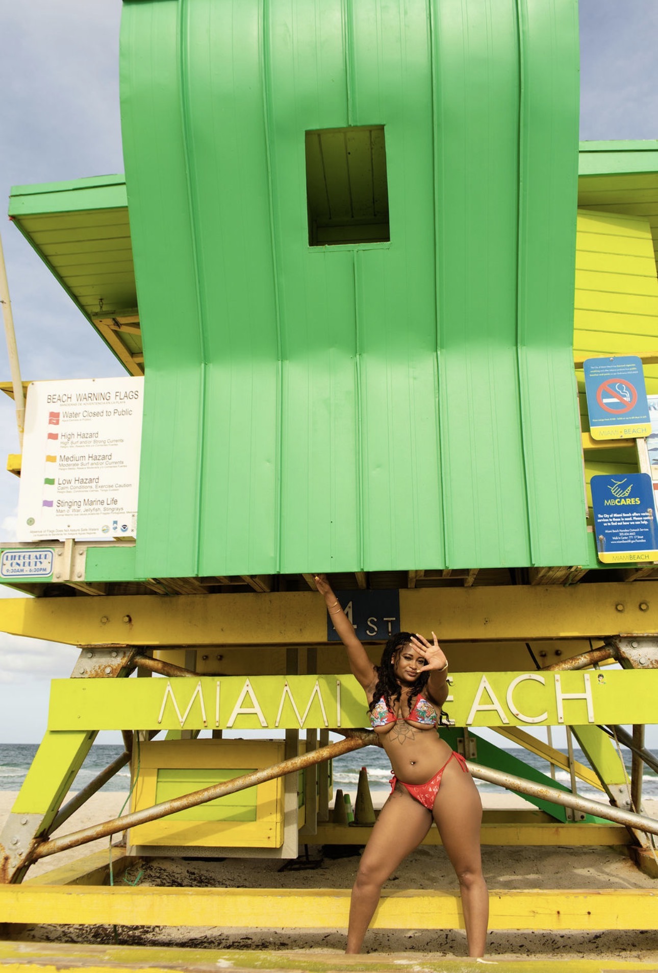 Person in a bikini standing on yellow stairs in front of a green and yellow structure, holding a paddle. Bright sky background.