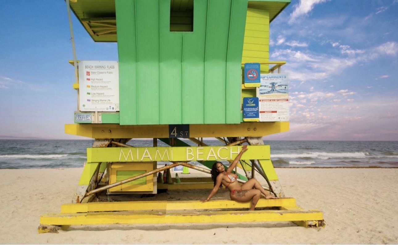 Colorful beach hut on Miami Beach with a person lying on the sand in front, ocean and sky in background.