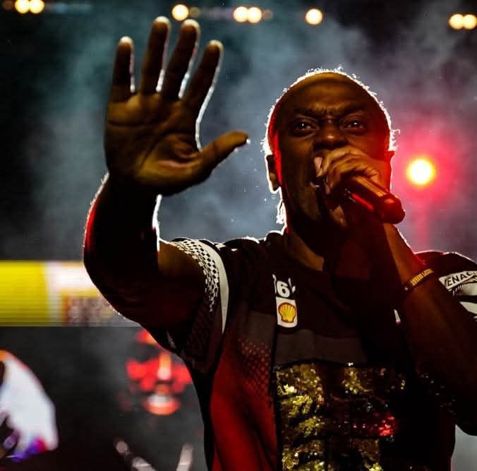 Person holding microphone with hand raised, stage lights in background, performing on stage.