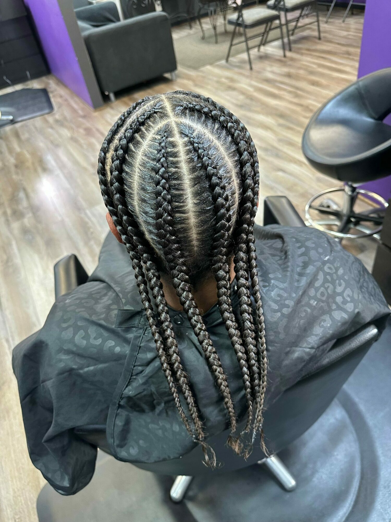 Top view of a person with braided hair sitting in a salon chair, with salon tools and furniture visible.