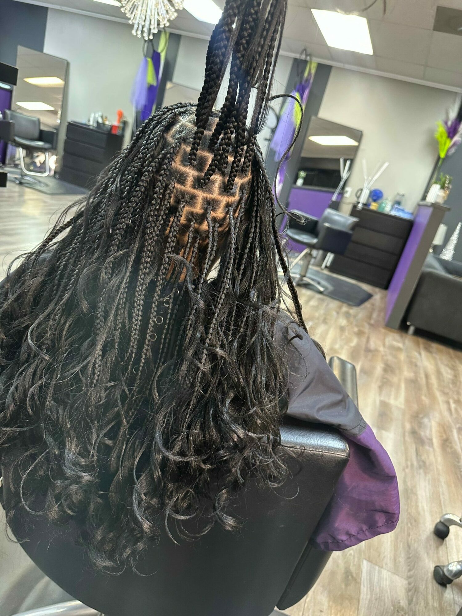 Person with long, curly hair sitting in a salon chair, facing away, with salon equipment visible in the background.