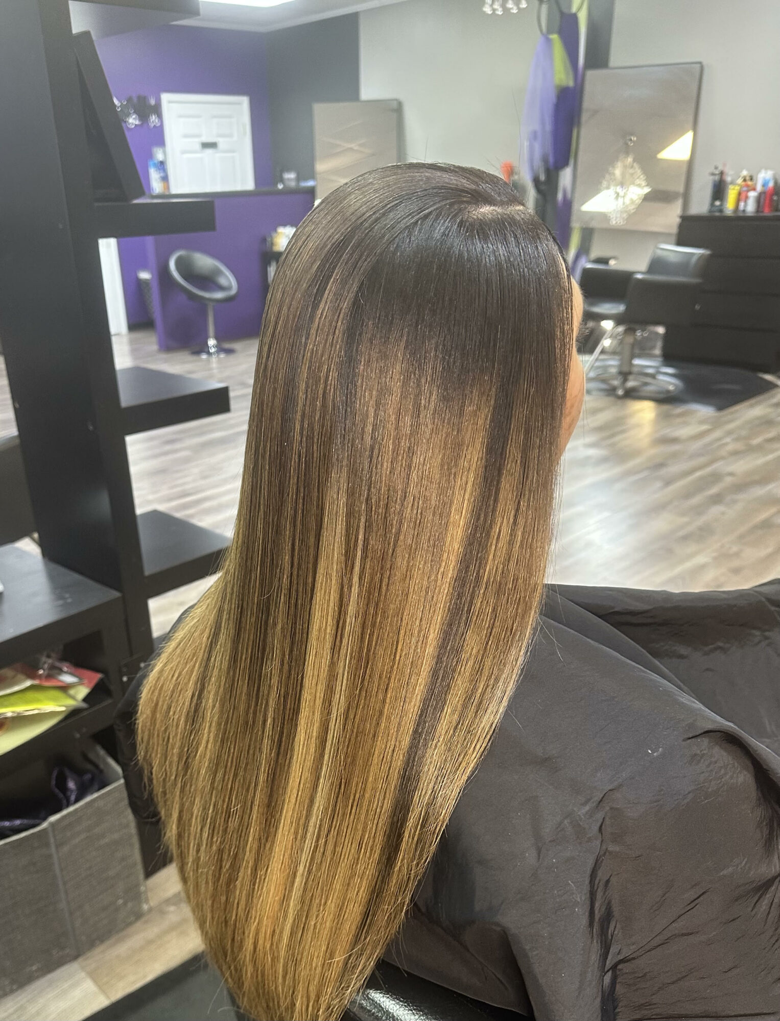 Person with long, straight hair in a salon, facing away, with a mirror and salon equipment in the background.