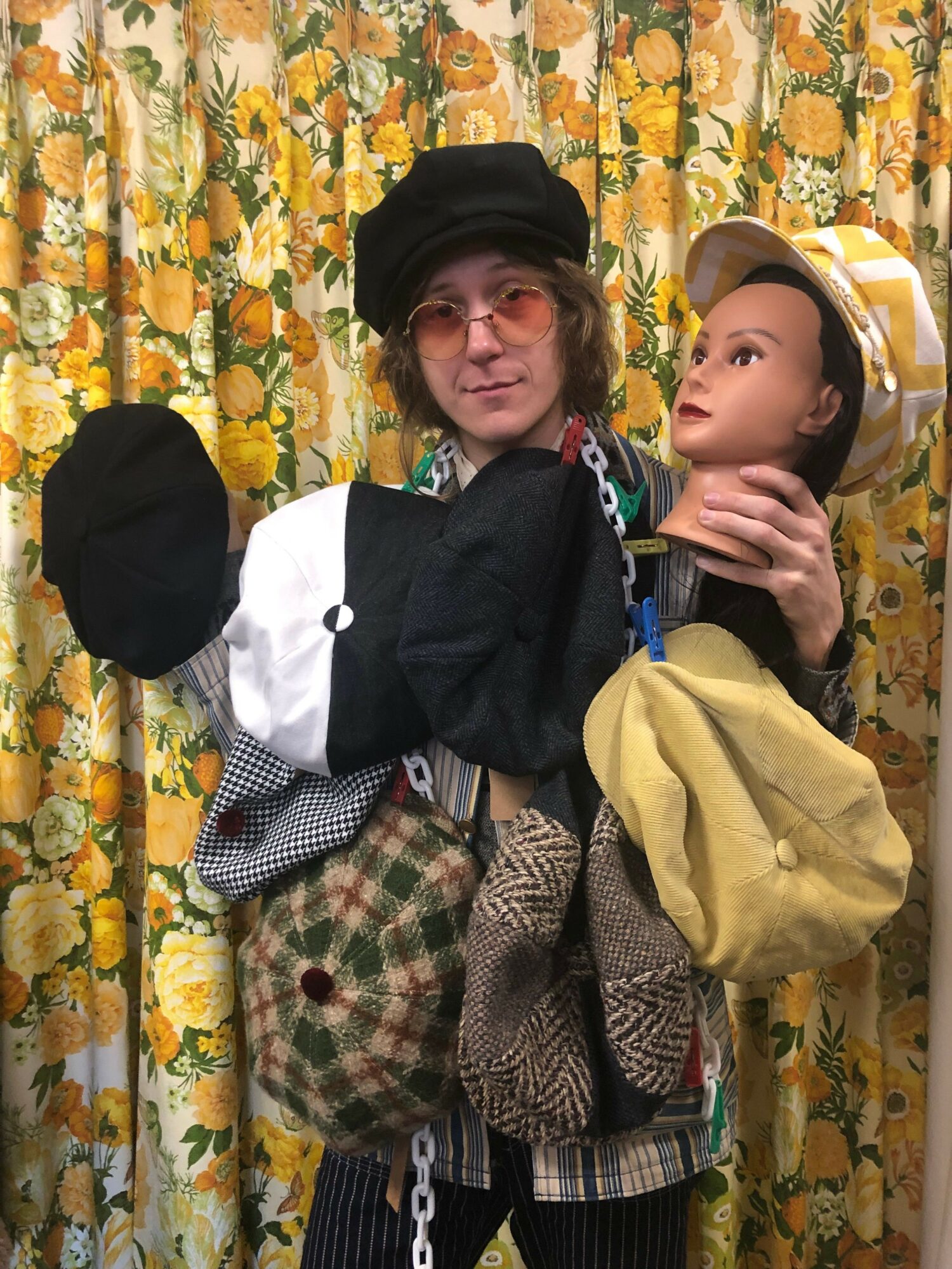 Two children sitting on a floral-patterned couch, one wearing a yellow hat and the other a black hat, with colorful clothing.