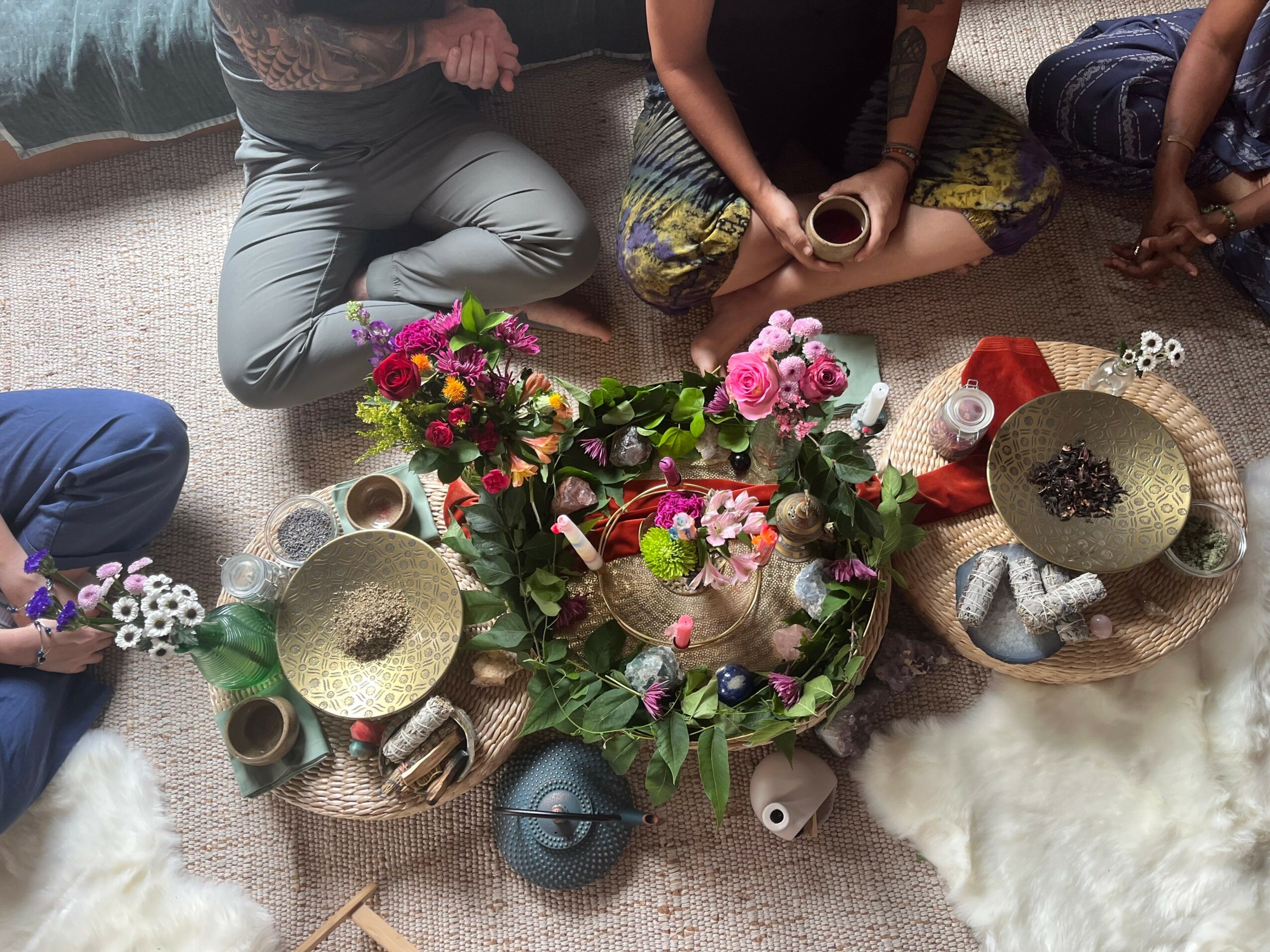 People sitting on the floor around flowers, candles, and bowls, preparing for a ceremony or gathering, viewed from above.