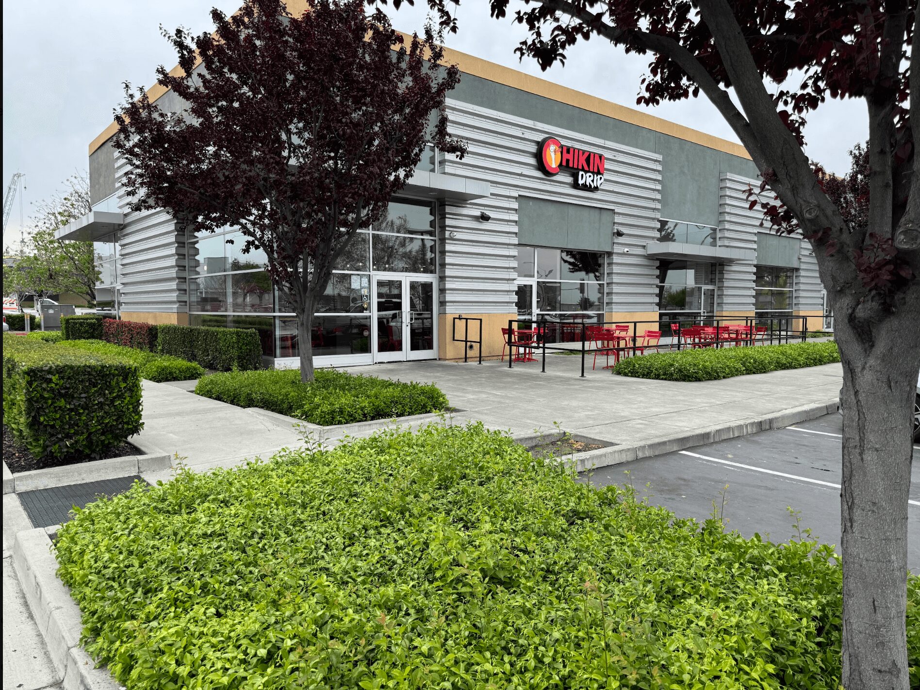 Exterior of a building with a sign, trees, bushes, and a parking lot in front.