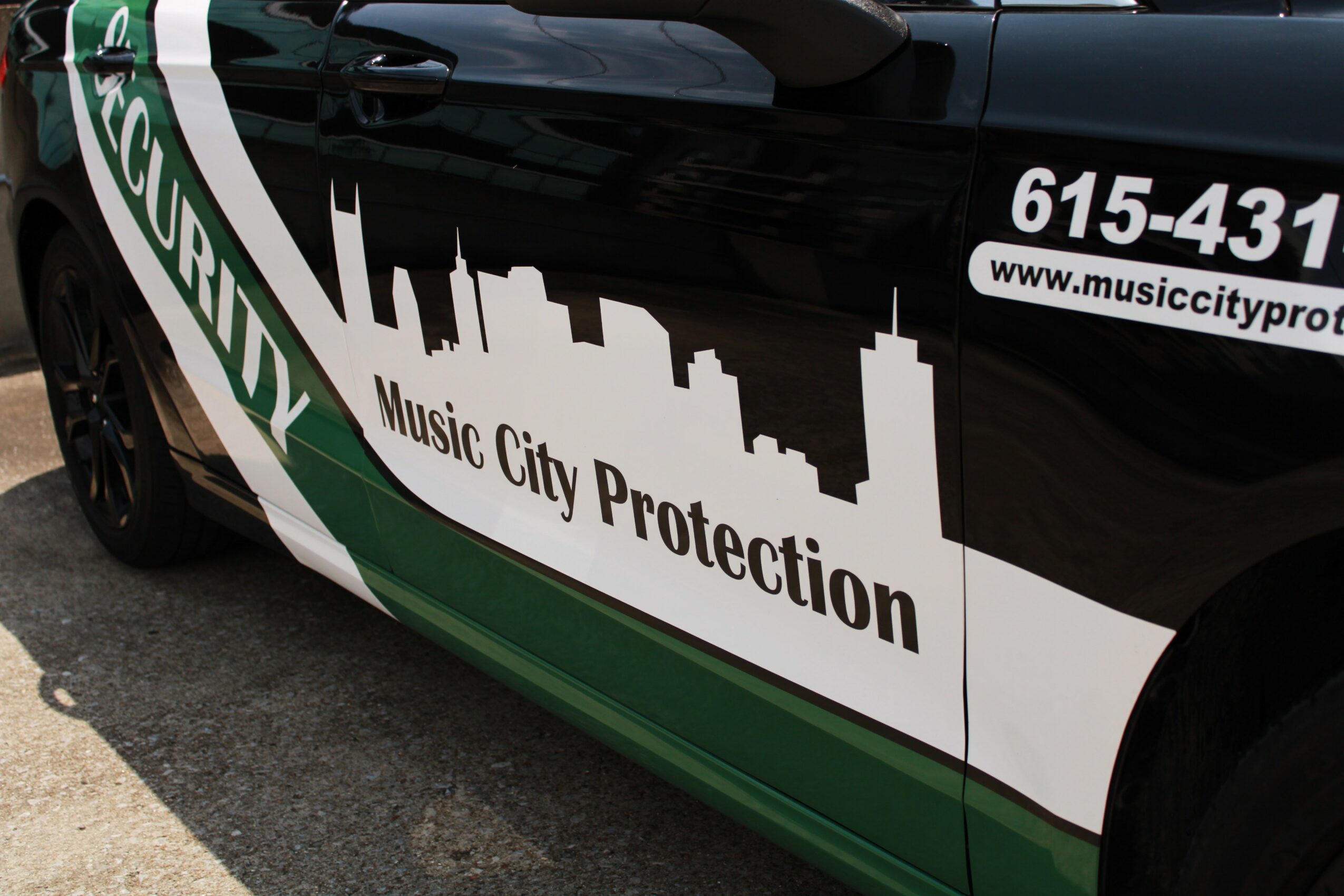 Close-up of a black vehicle with a green and white logo for Music City Protection, showing part of the city skyline and contact info.