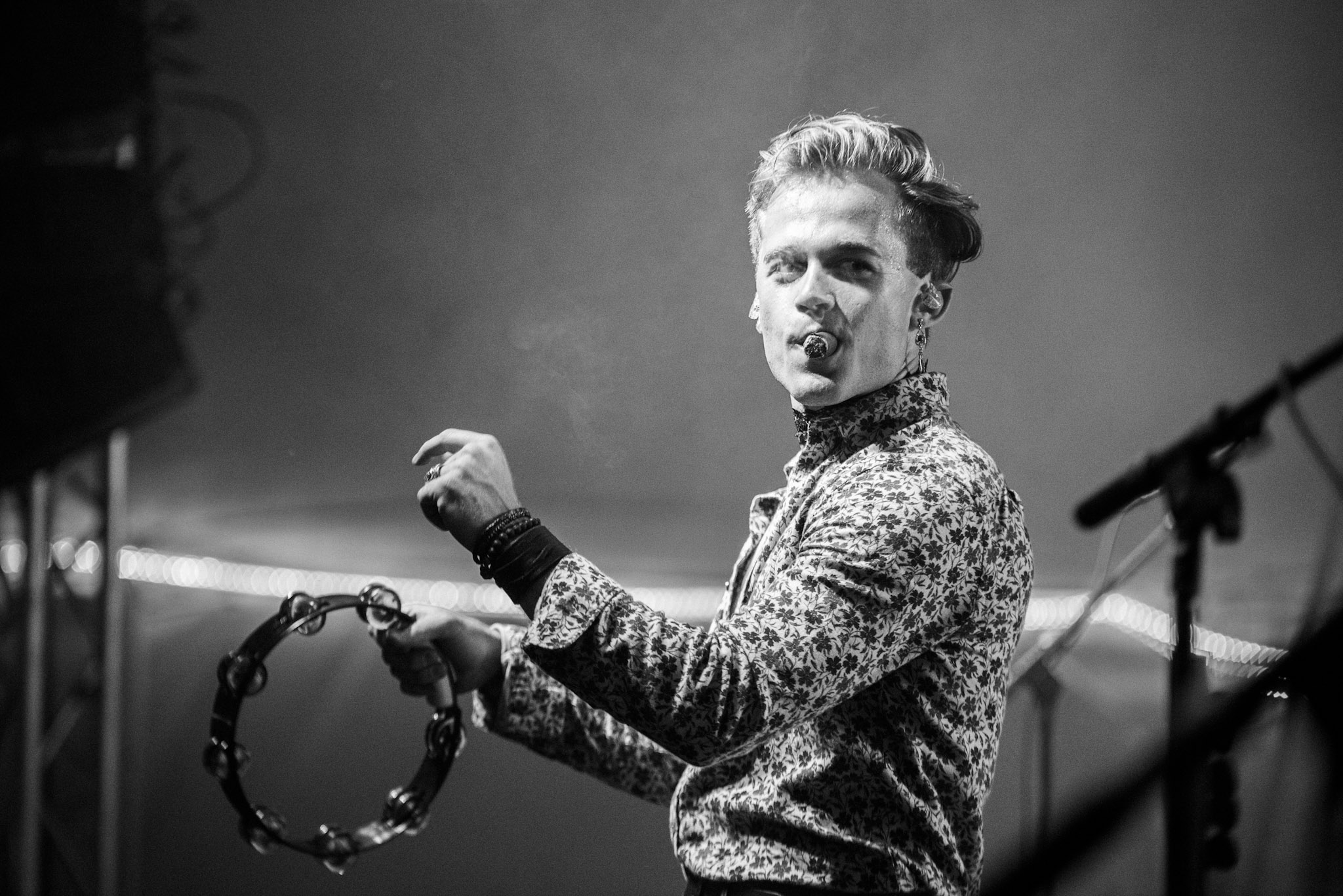 Black and white photo of a person holding a tambourine, standing on stage with a microphone in the background.