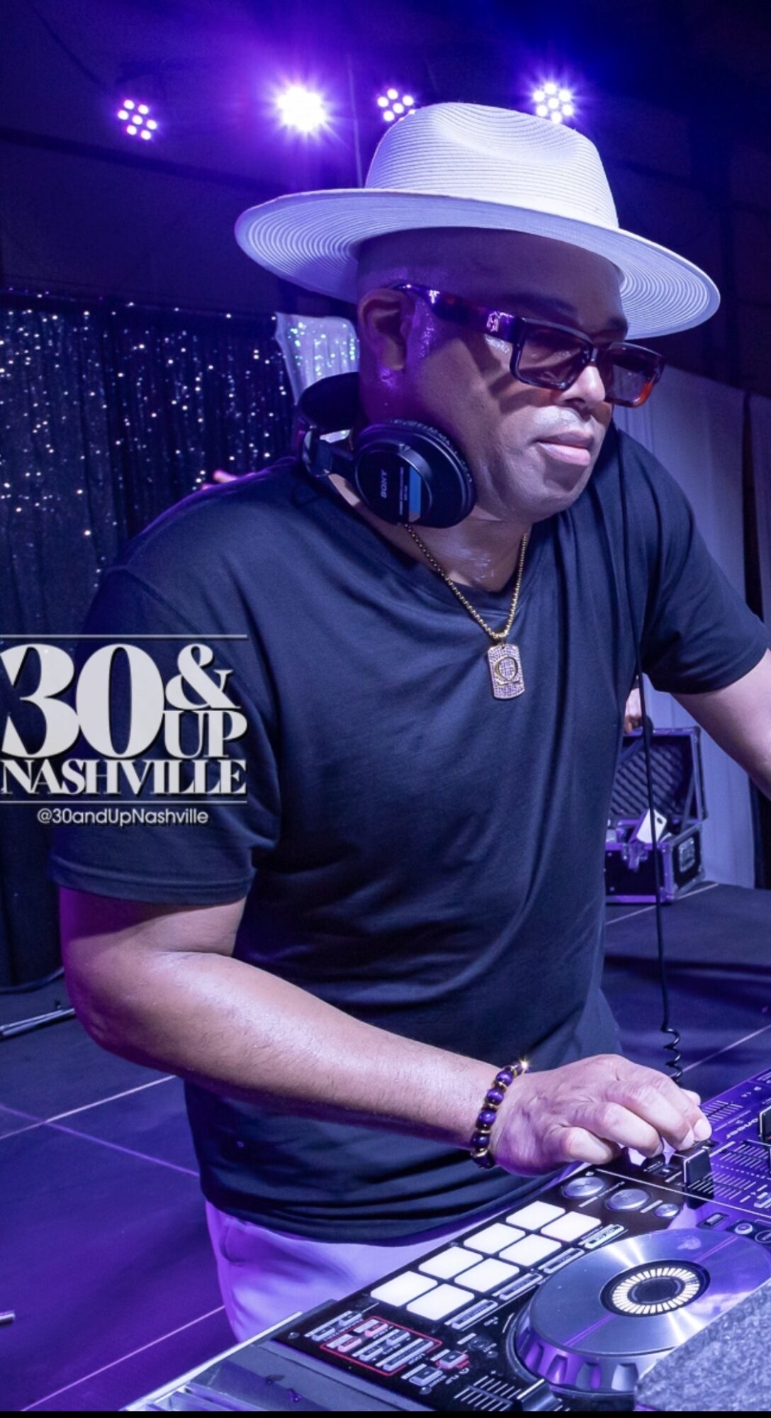 DJ wearing a white hat, sunglasses, and headphones, working at a DJ booth with colorful lights in the background.