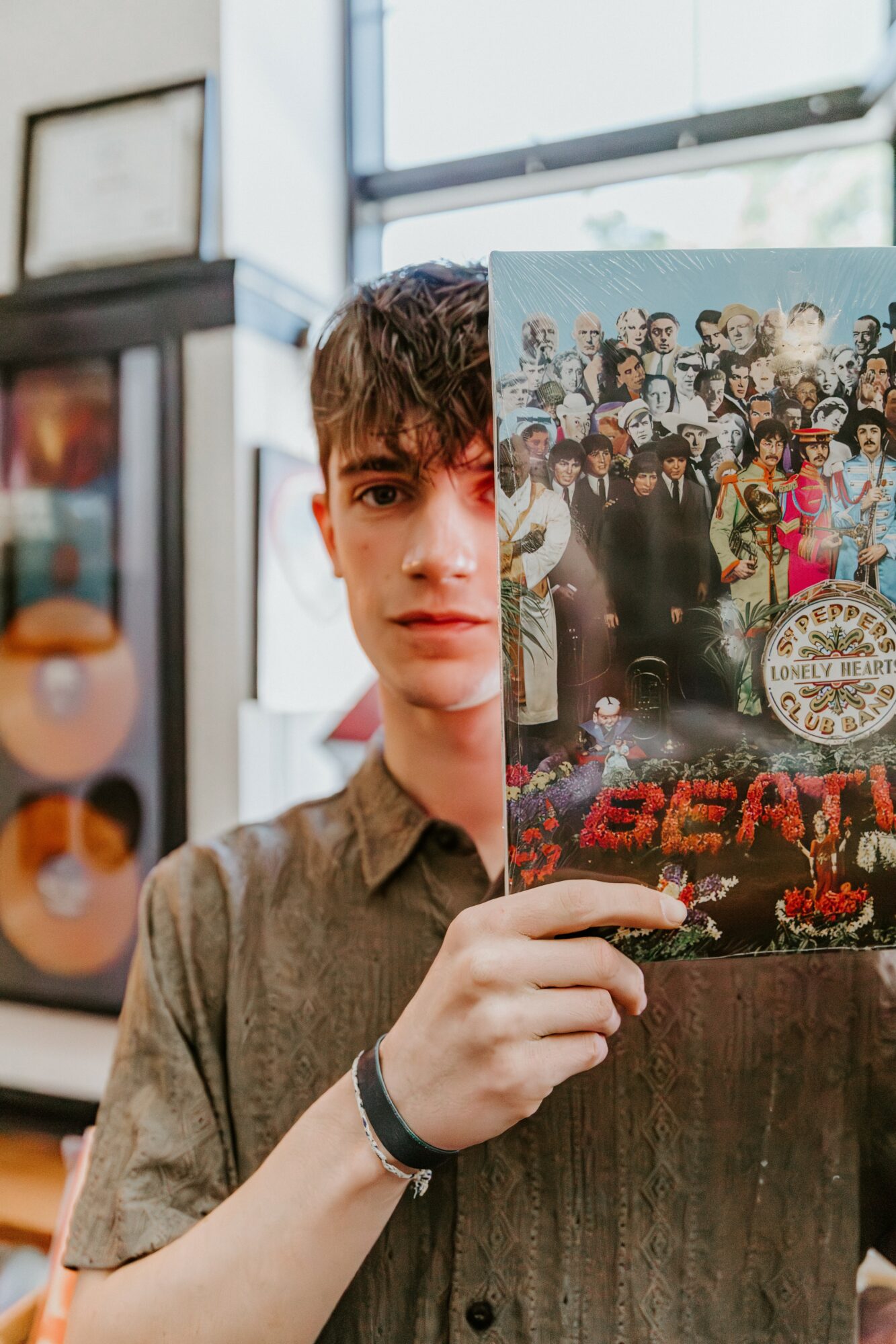 Young person holding a poster with a group photo, partially obscuring their face, in an indoor setting with windows.
